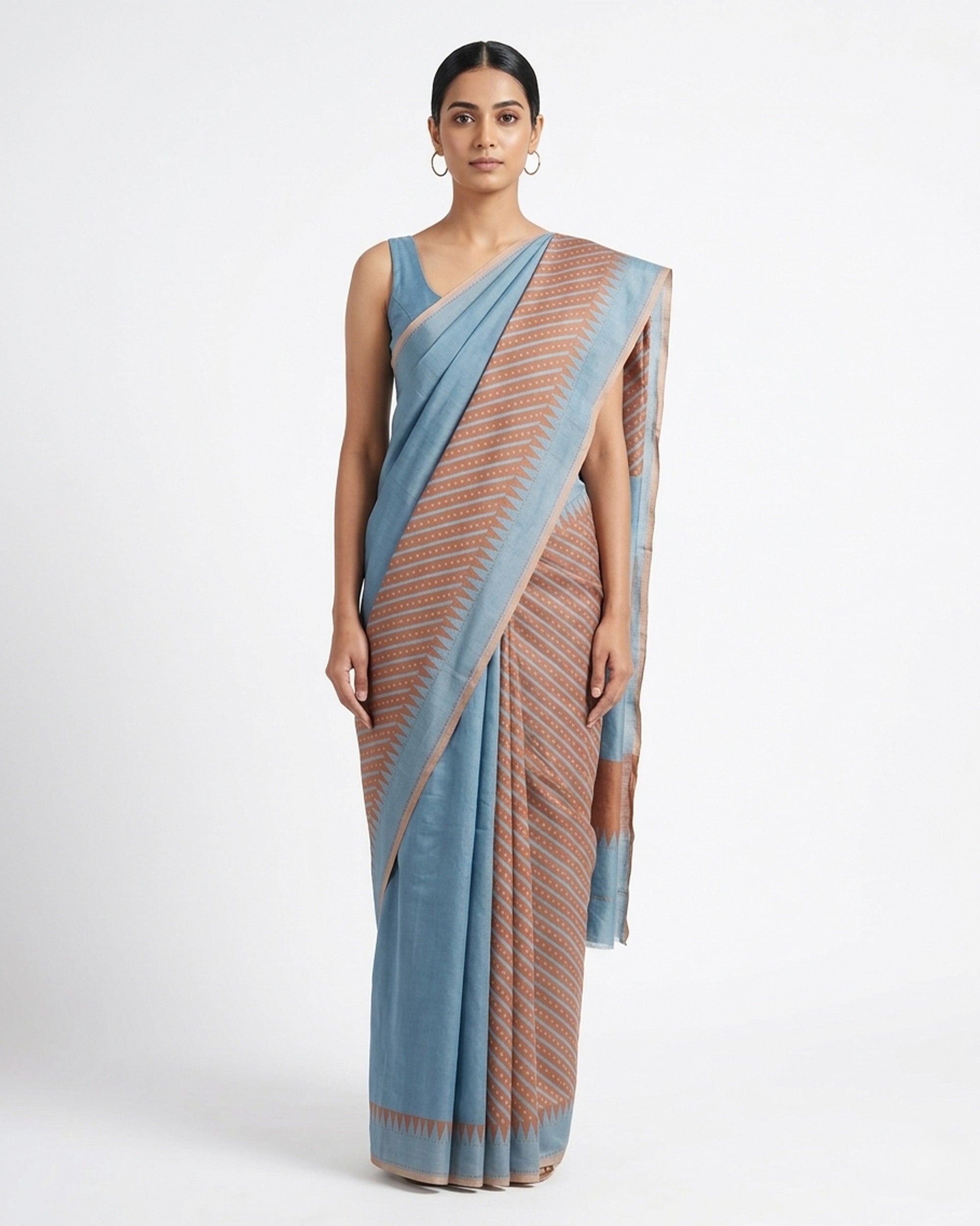A woman wearing a dual-toned blue and brown textured linen saree with a sleeveless blue blouse, draped elegantly against a white background.