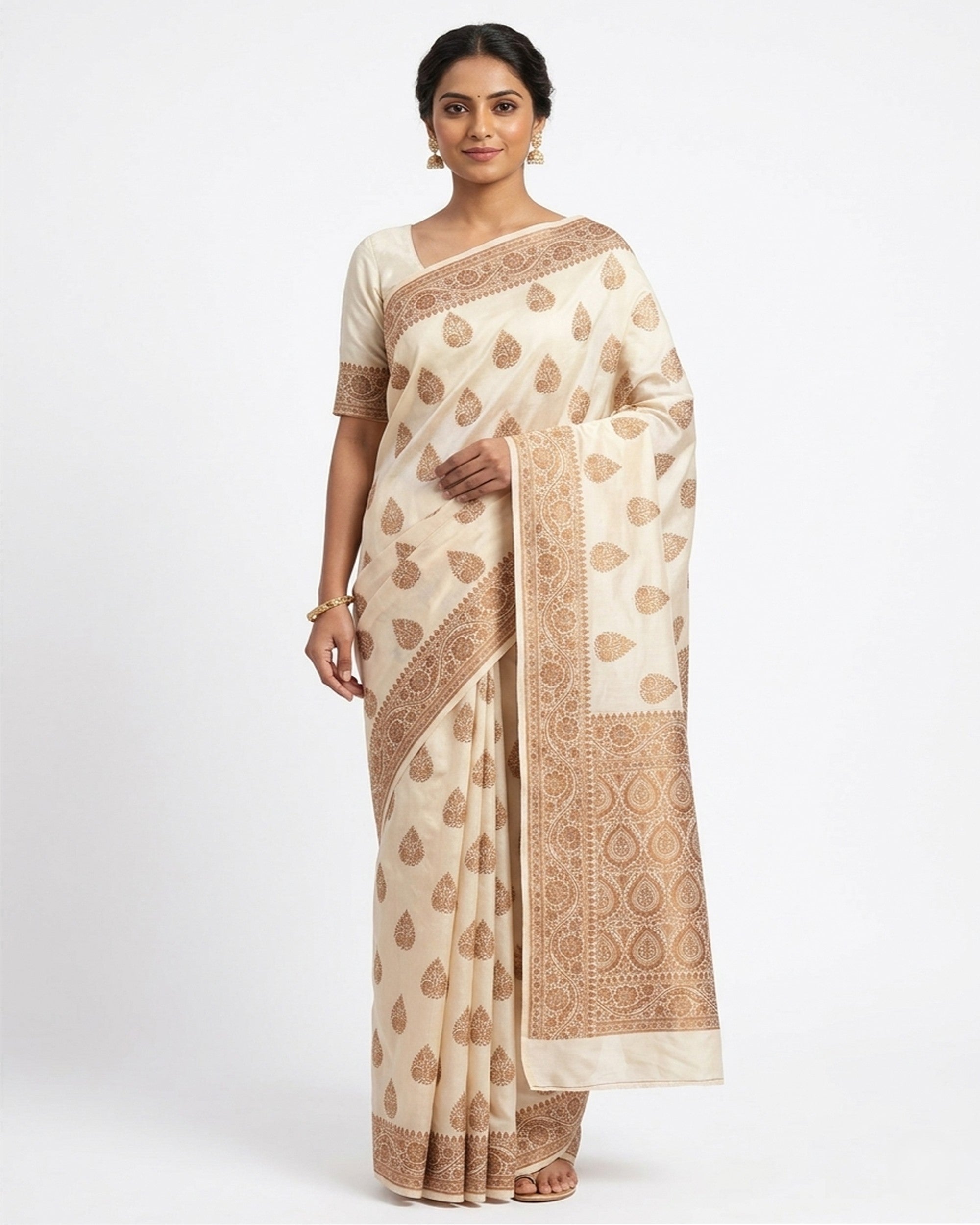 A woman elegantly posing in an off-white & gold-toned woven Banarasi silk saree from The Weaver's Shop, featuring traditional floral Zari motifs, an ornate heavy border, and a matching silk blouse against a clean white background.
