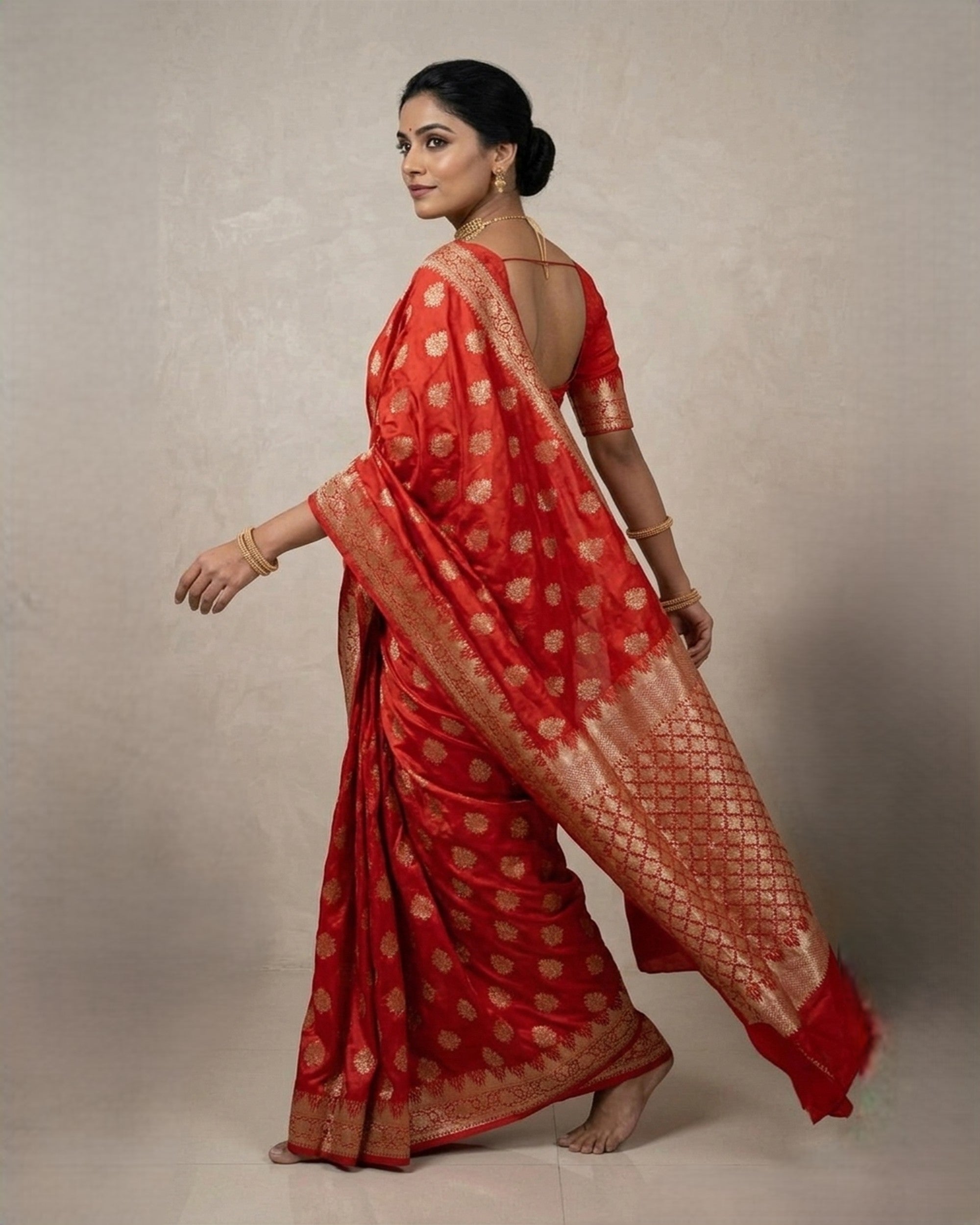 A woman wearing a vibrant red Banarasi silk saree with intricate gold zari floral patterns and a broad, decorative border, posed against a plain white background.