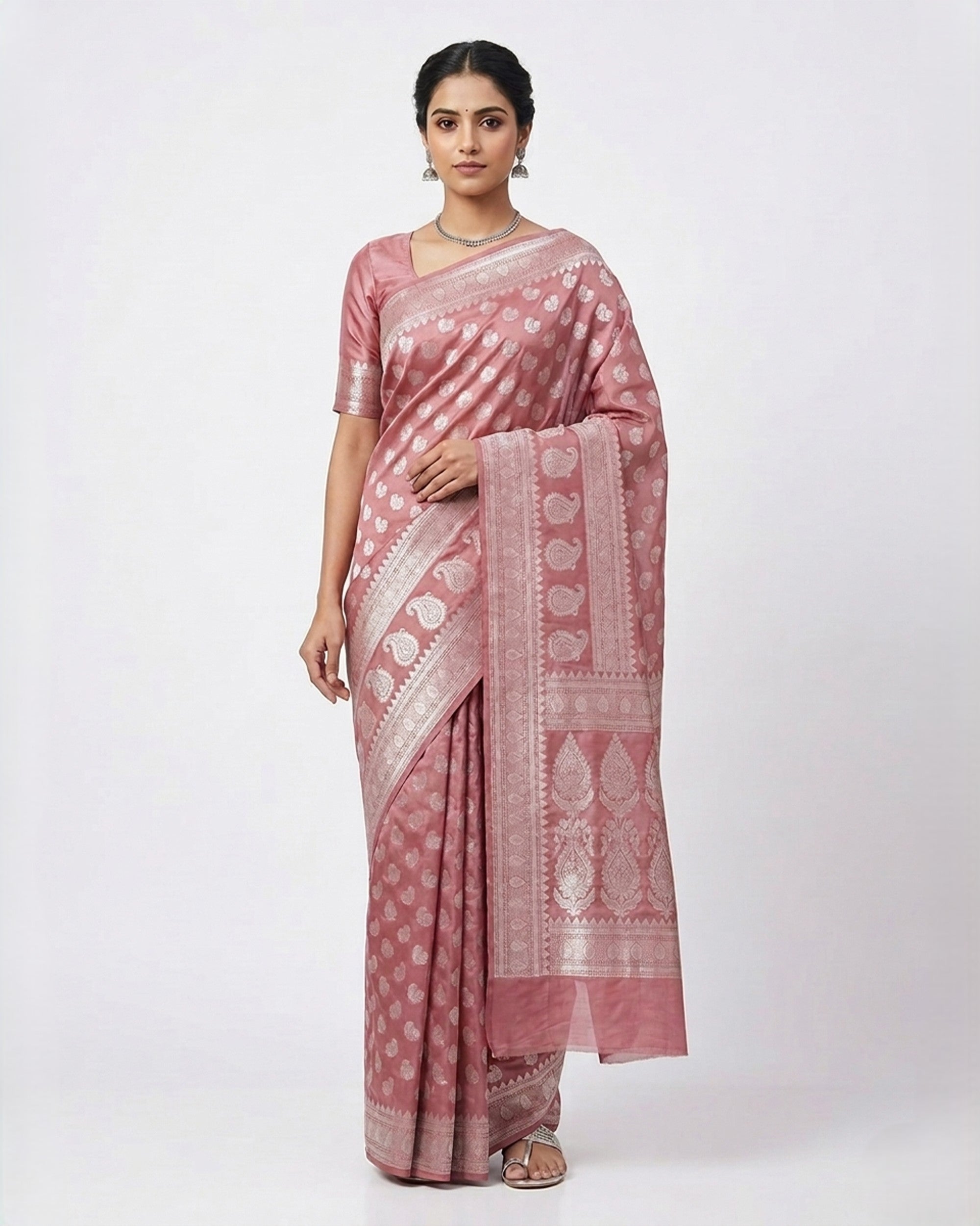 A woman gracefully modeling a Dusty Rose & Silver Woven Banarasi Silk Blend Saree from The Weaver's Shop, featuring all-over silver Zari ethnic motifs, a majestic silver border, and a matching woven blouse against a white background.