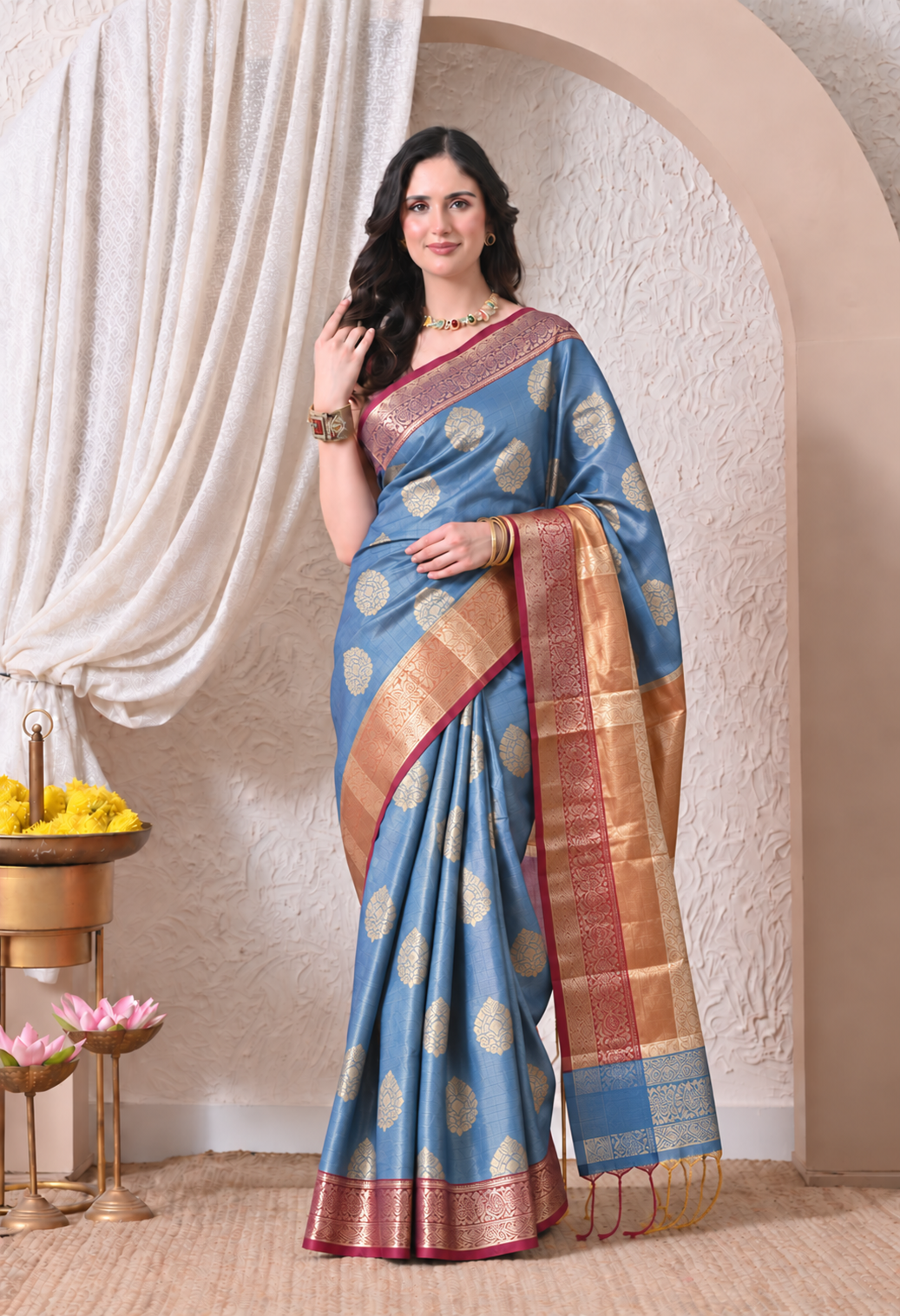 Woman wearing a powder blue and gold woven zari silk blend saree with a contrasting woven border and tassels.
