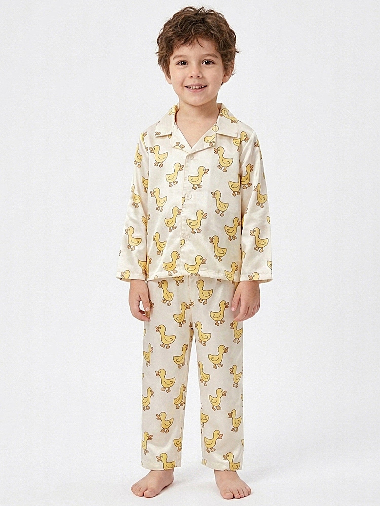 Young boy smiling while wearing a cream-colored, satin cartoon duck print pajama set.