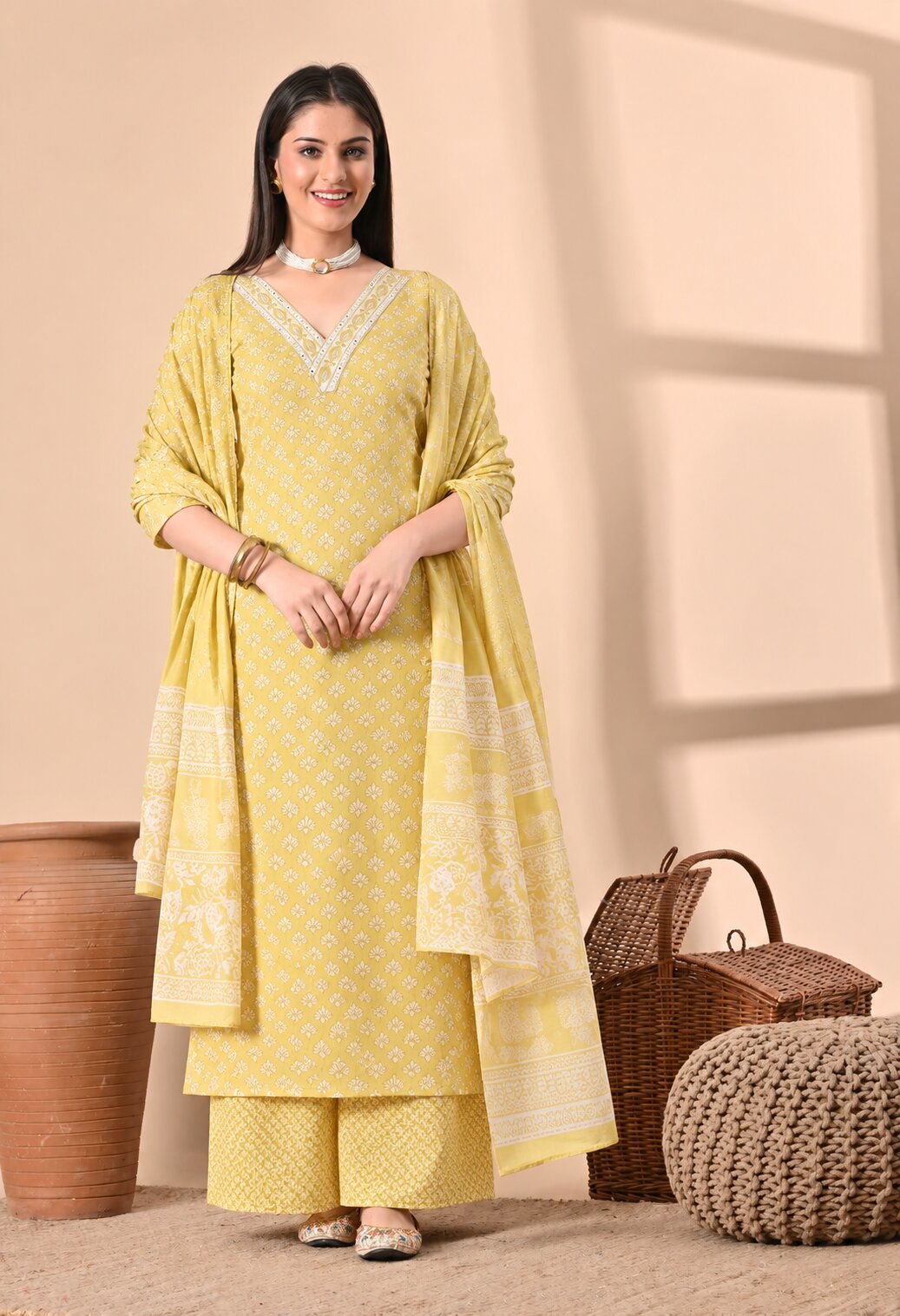 Mustard yellow ethnic suit set featuring a white printed V-neck kurta with delicate geometric motifs, matching wide-leg pants, and a coordinating dupatta with white printed patterns and decorative borders.