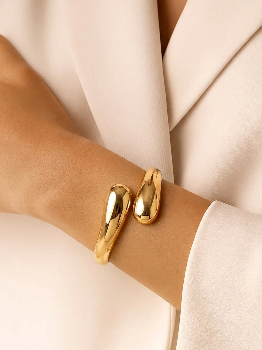 A sleek, gold-tone crossover hinged bangle with a high-polish finish, shown vertically on a white background.
