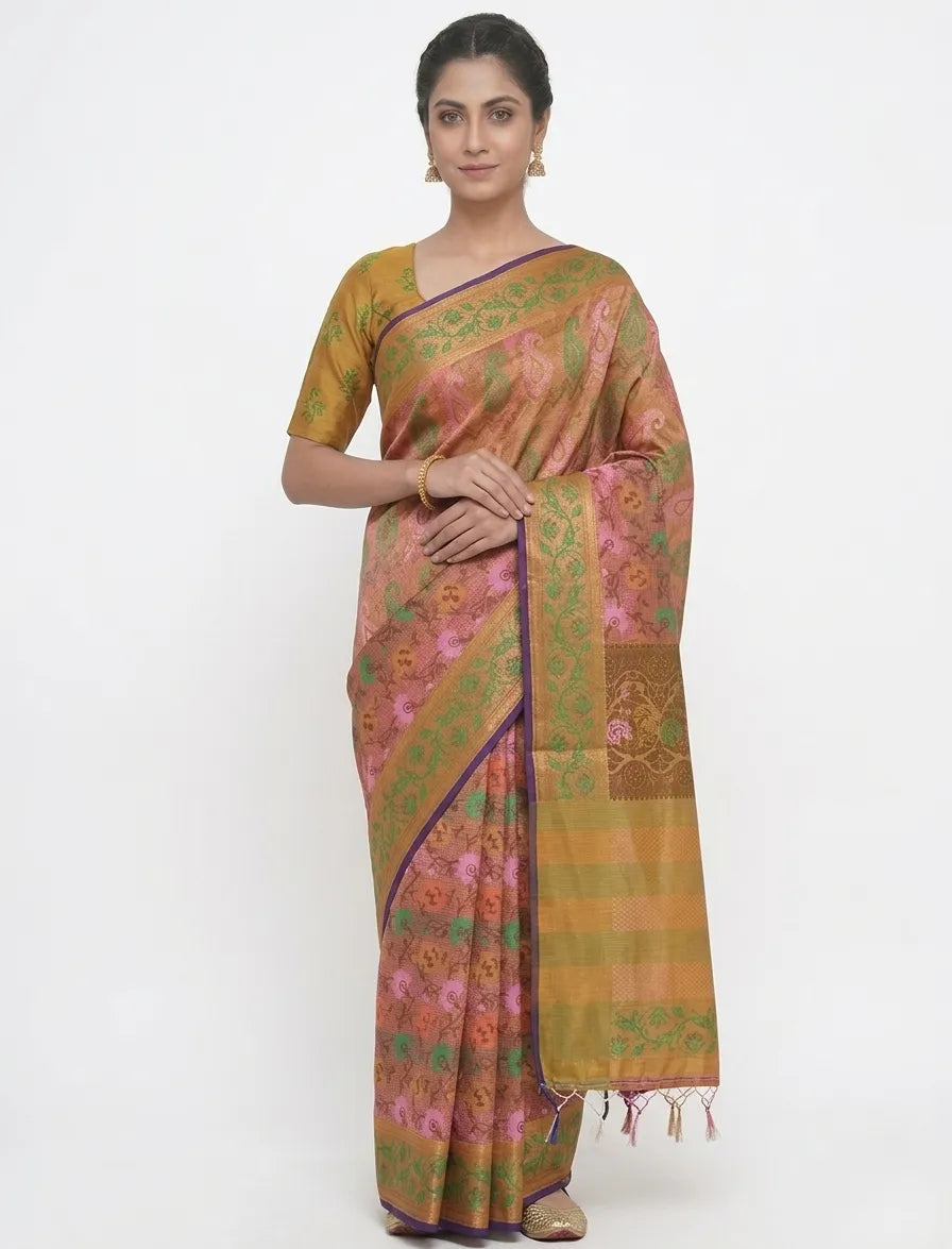 A woman in a mustard yellow and pink floral printed silk blend saree featuring a green zari border with purple piping and handcrafted tassels on the pallu.
