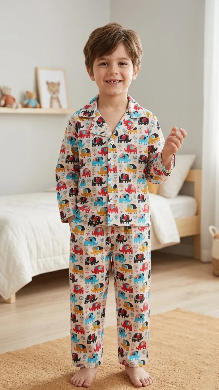 A smiling young boy standing in a bedroom, wearing a white notched-collar pajama set featuring a vibrant, multi-colored transport and vehicle print including cars and buses.