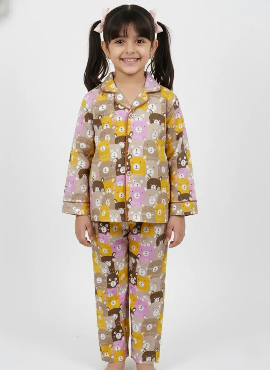 A young girl standing against a white background, wearing a yellow long-sleeved pajama set with a playful multi-colored animal print