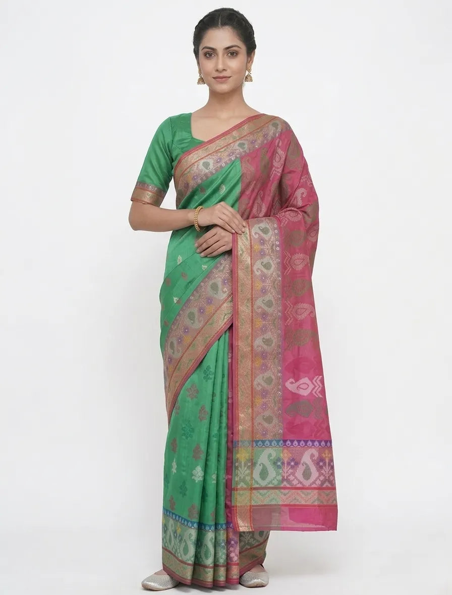 A woman in an emerald green and magenta Banarasi art silk saree with woven ethnic motifs, a gold zari border, and a matching green blouse.