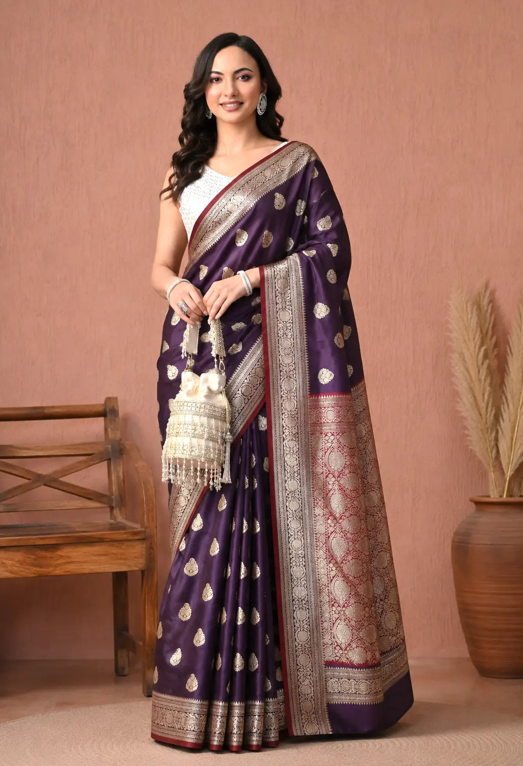 Woman wearing a deep purple silk blend saree adorned with gold zari motifs, featuring a decorative border and contrast pallu.
