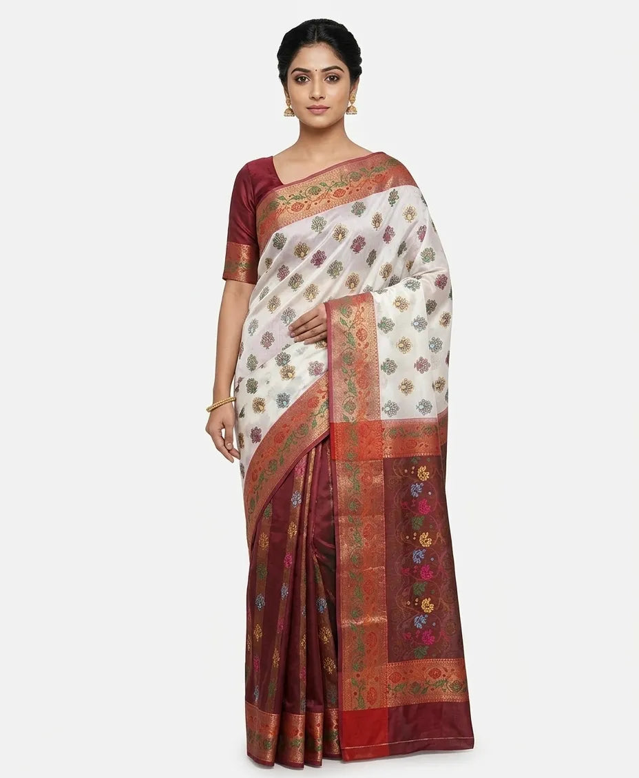 An Indian woman modeling an off-white silk blend saree with floral woven buttas and a contrasting maroon pallu and pleated section. She wears a maroon blouse and gold earrings against a plain white background.
