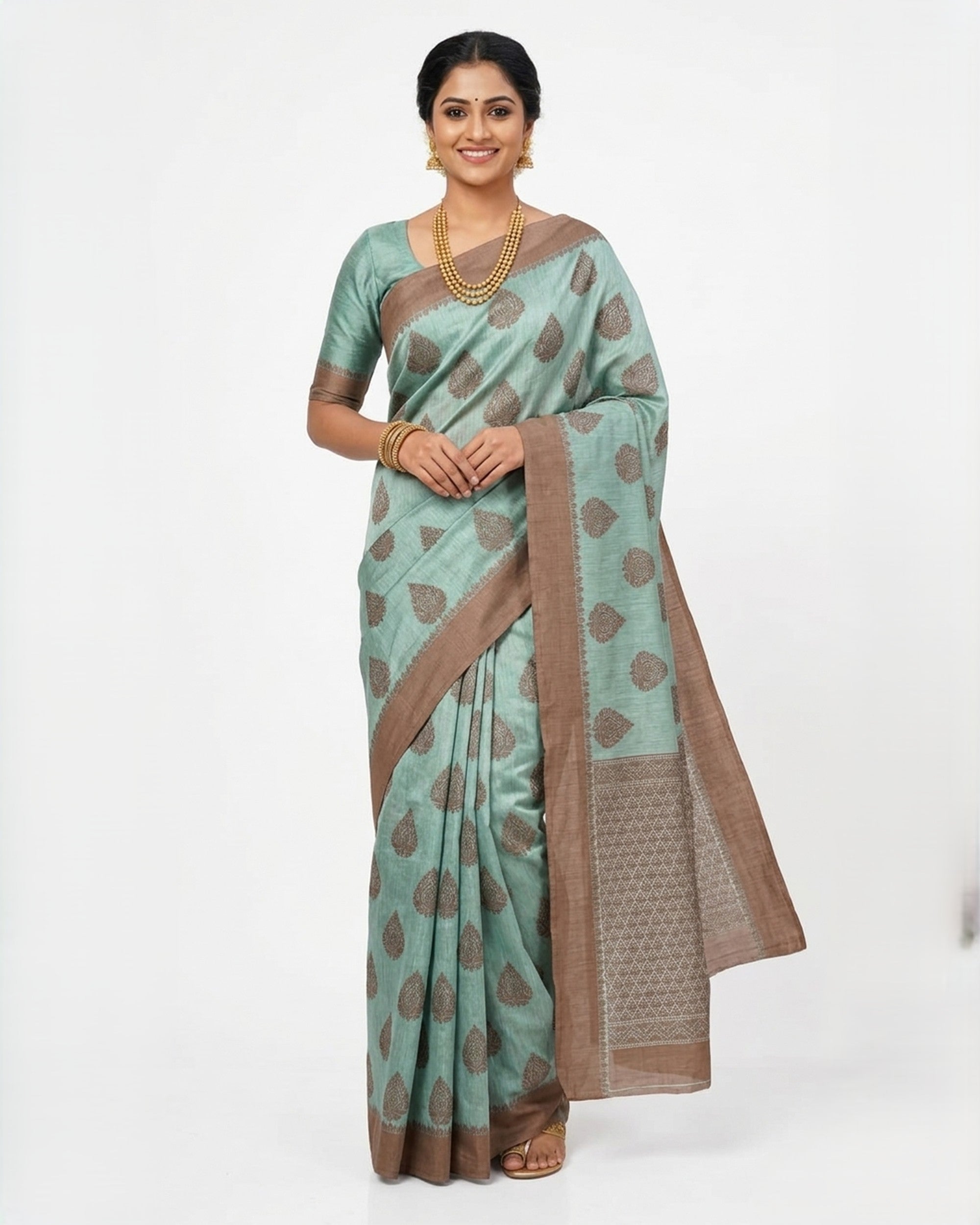 A woman wearing a seafoam green Banarasi silk saree featuring copper-toned floral motifs and a broad, intricate copper zari border, posed against a plain white background.