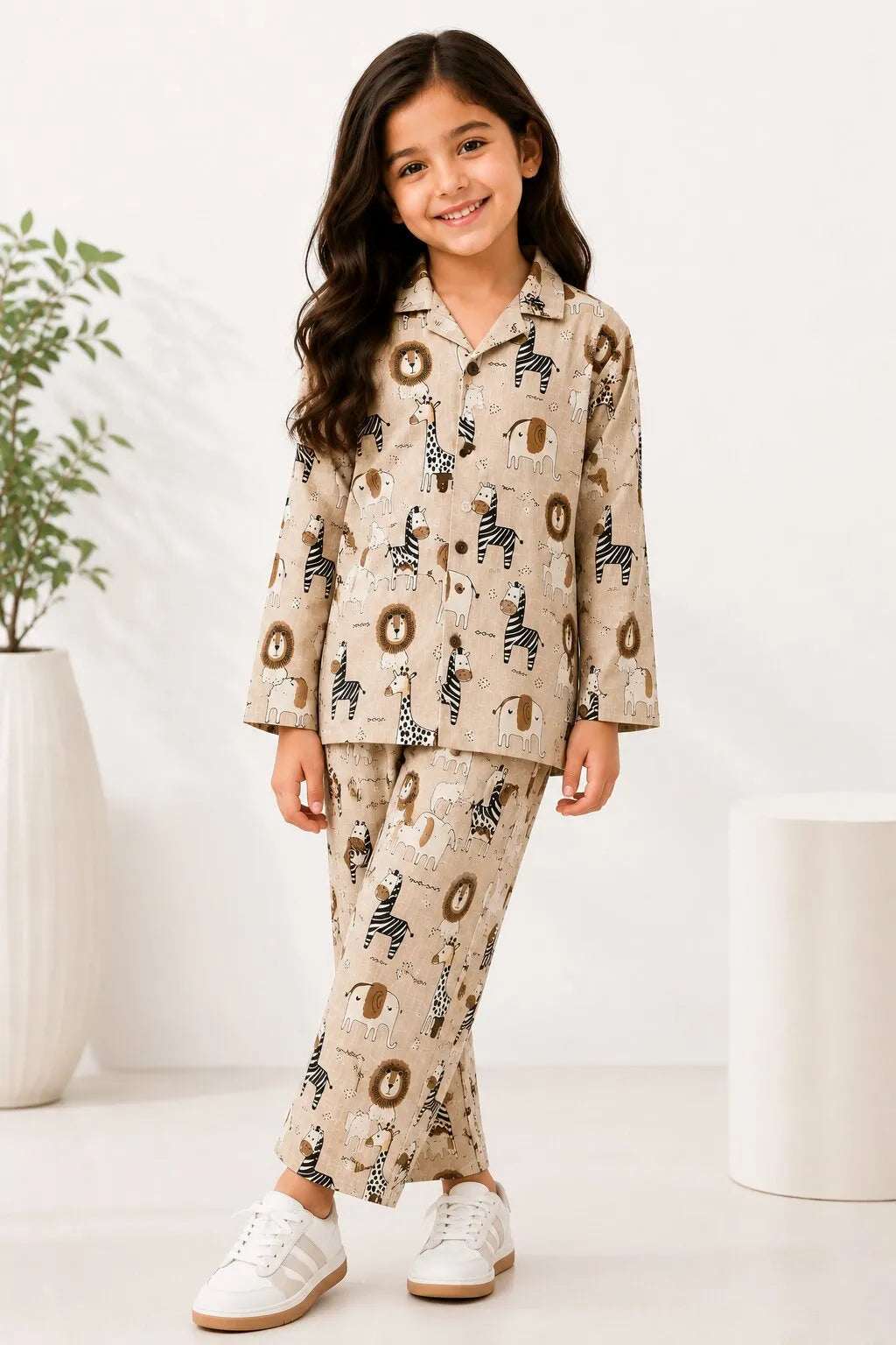 A young girl modeling a beige, long-sleeved pajama set featuring an all-over brown animal print, standing against a plain white background.
