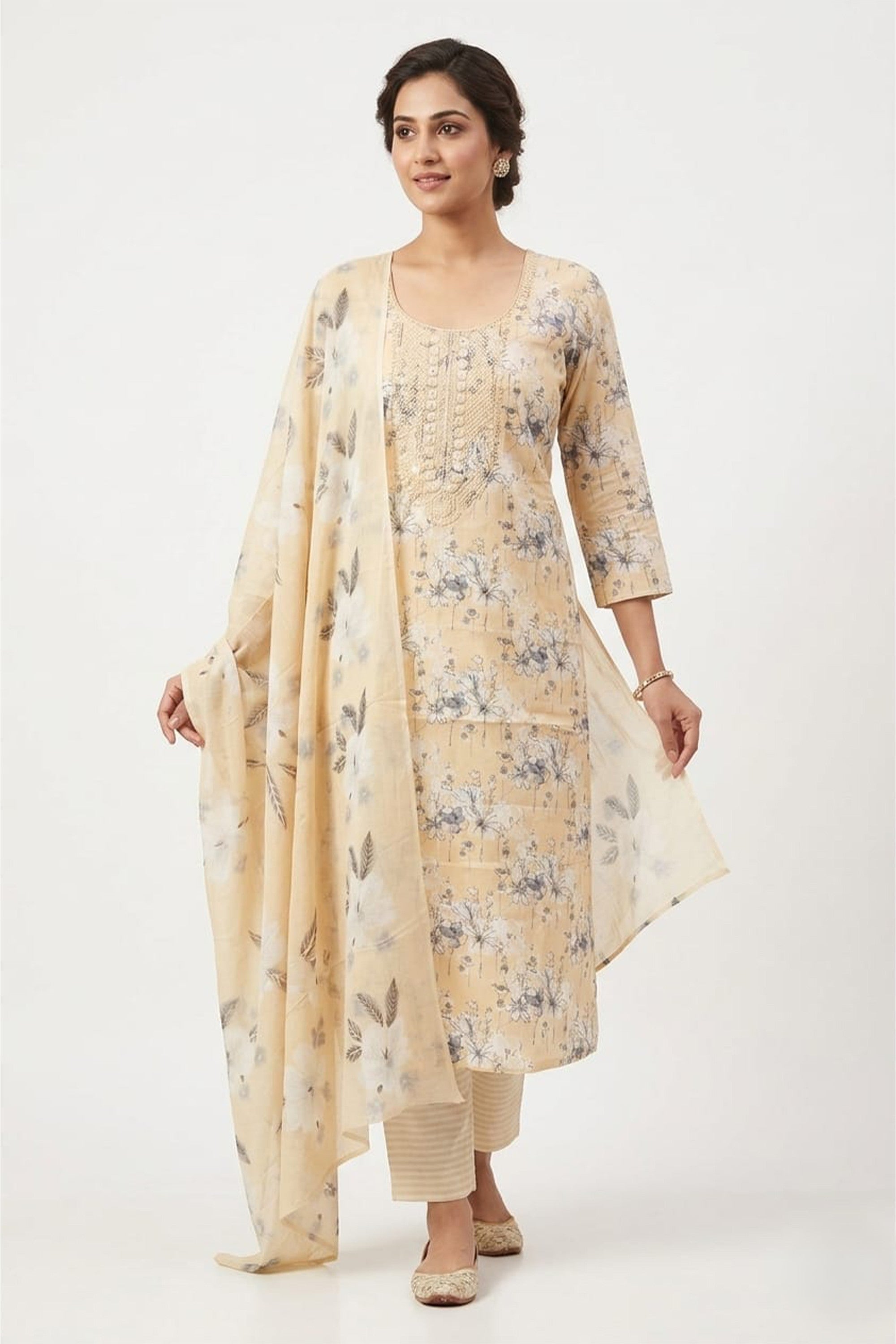 A cream-colored cotton unstitched suit with white and grey floral prints and an embroidered neckline, shown with a matching dupatta and striped bottom.
