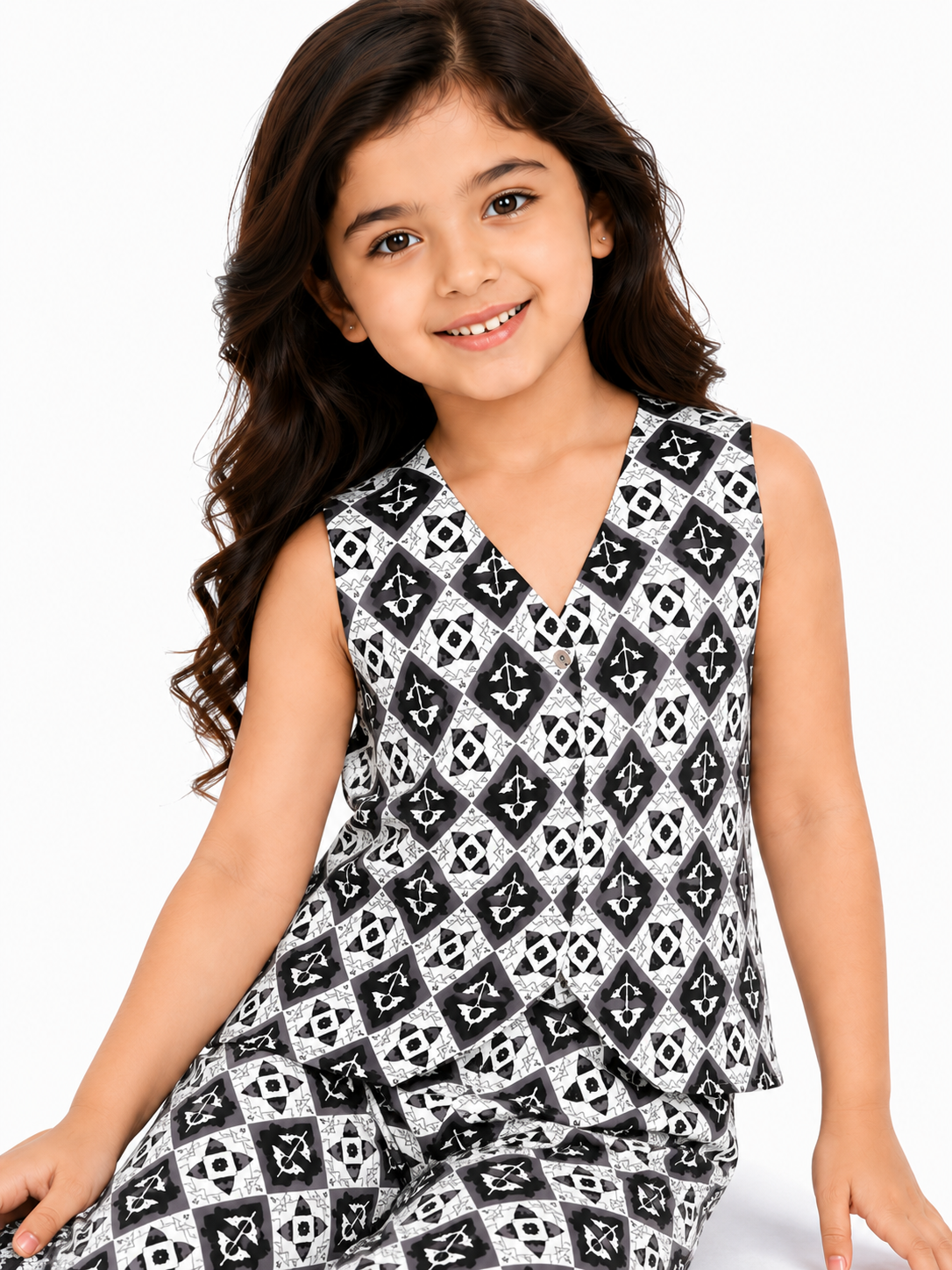 A young girl smiling while posing in a black and white monochromatic geometric print pure cotton co-ord set, featuring a sleeveless vest-style buttoned top and relaxed wide-leg trousers
