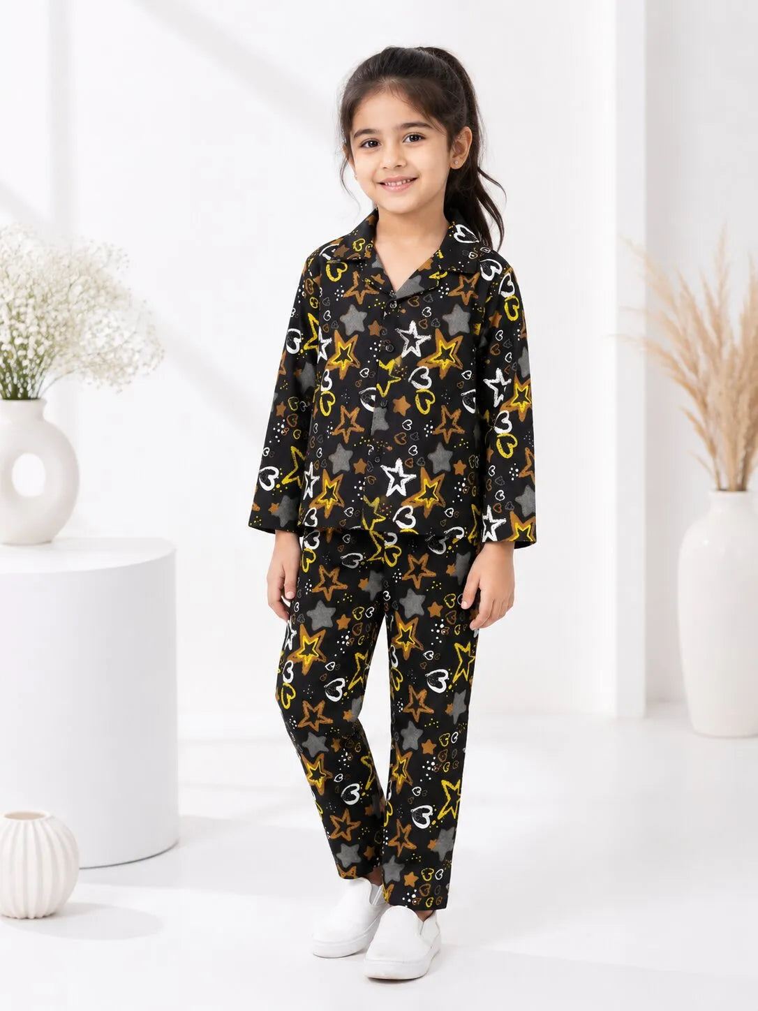 A child smiling while wearing a black cotton night suit featuring a yellow star and white heart print.