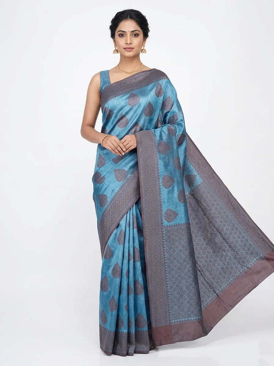 Woman in a blue Banarasi silk blend saree with grey leaf motifs and a dark grey Zari border, posing against a white background.