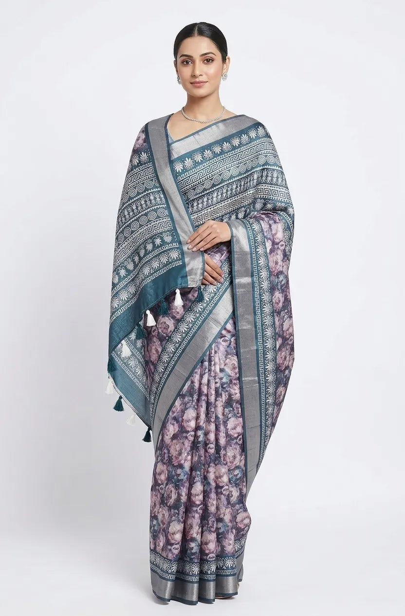 A woman modeling a blue and lavender floral printed silk blend saree, featuring a silver zari border and a teal patterned pallu with hanging tassels.
