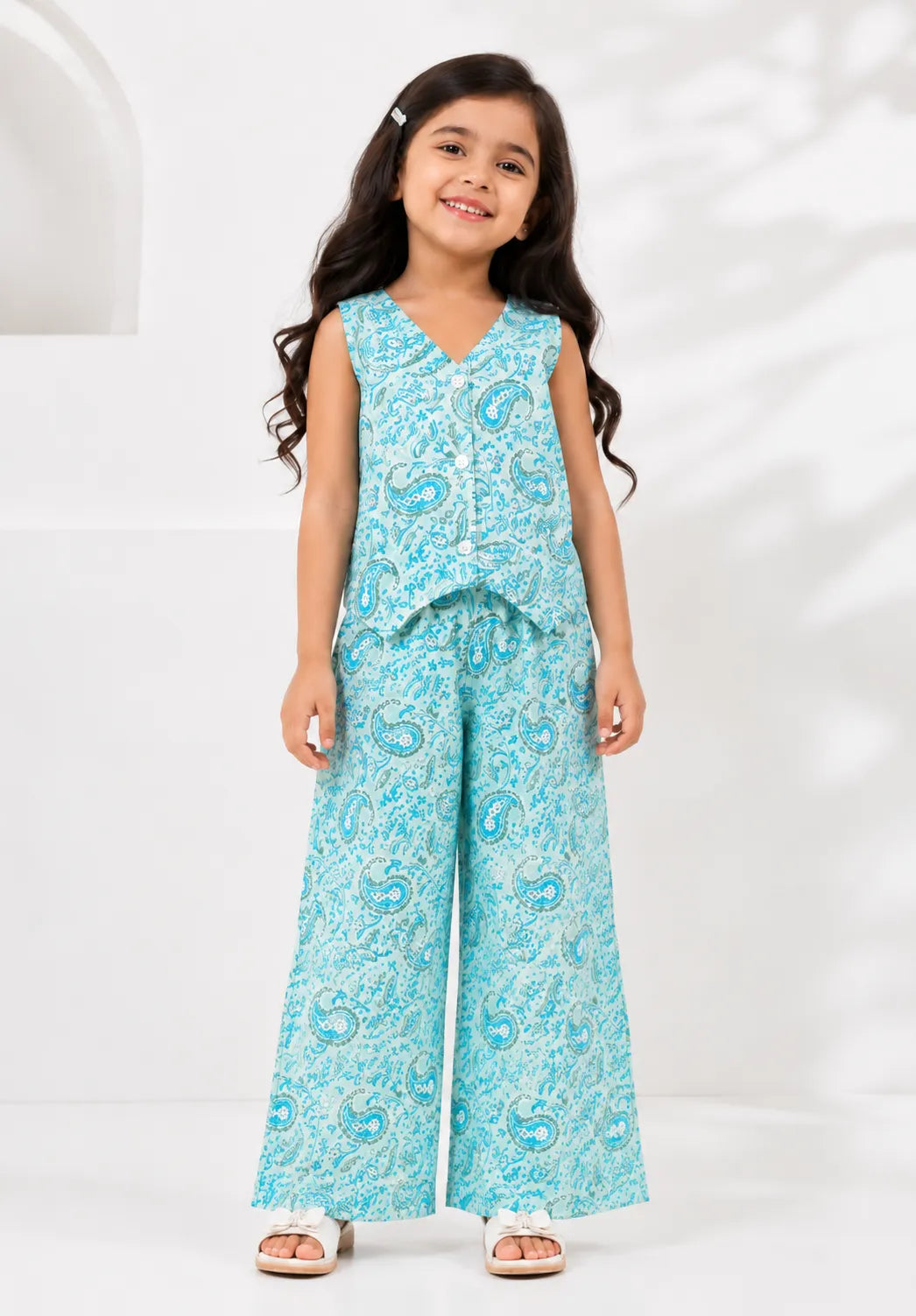 Young girl wearing an aqua blue paisley printed sleeveless vest and matching wide-leg pants co-ord set.
