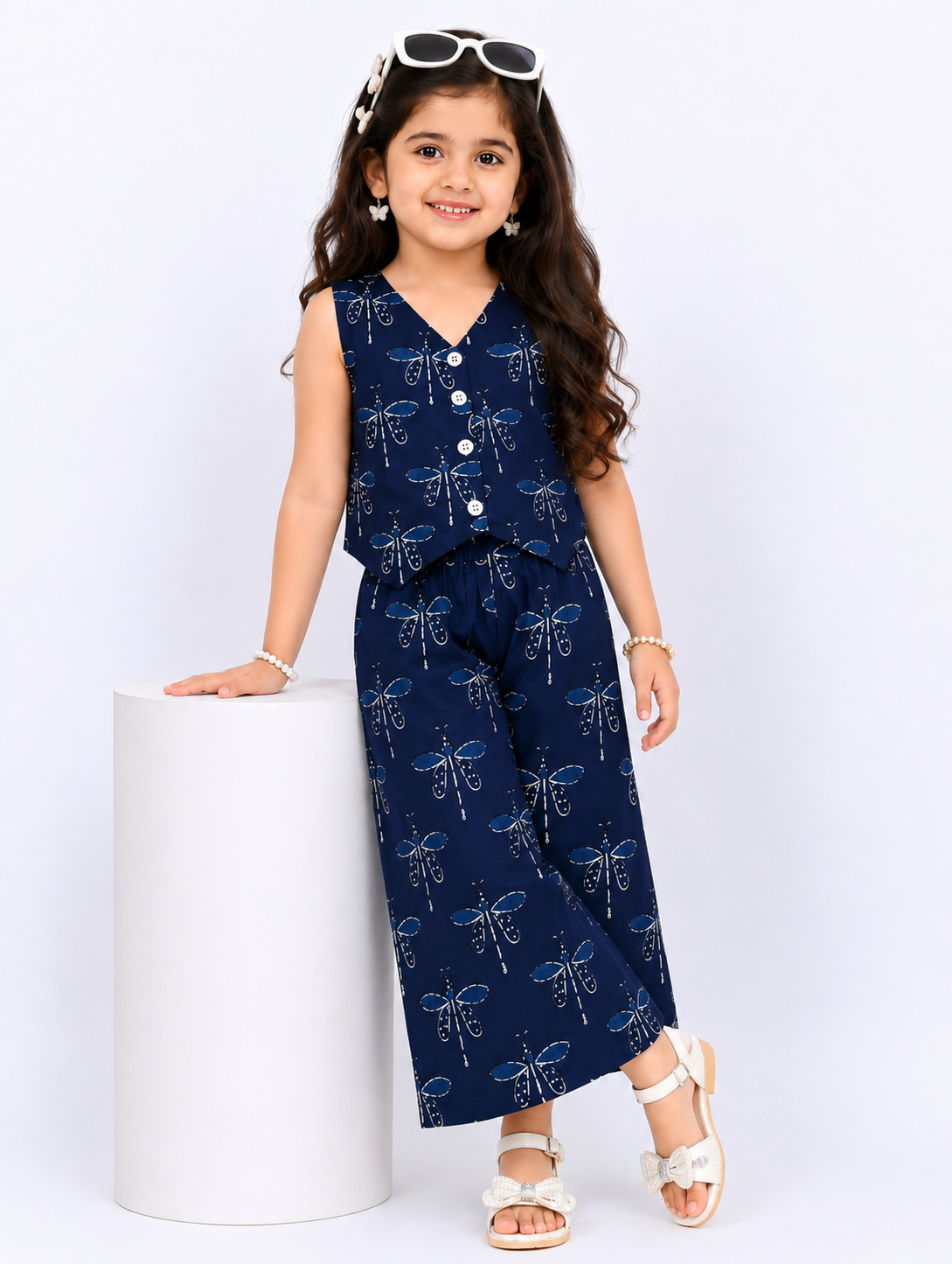 A young girl smiling in a pink pure cotton co-ord set featuring a red floral and paisley print, consisting of a sleeveless vest-style buttoned top and wide-leg trousers
