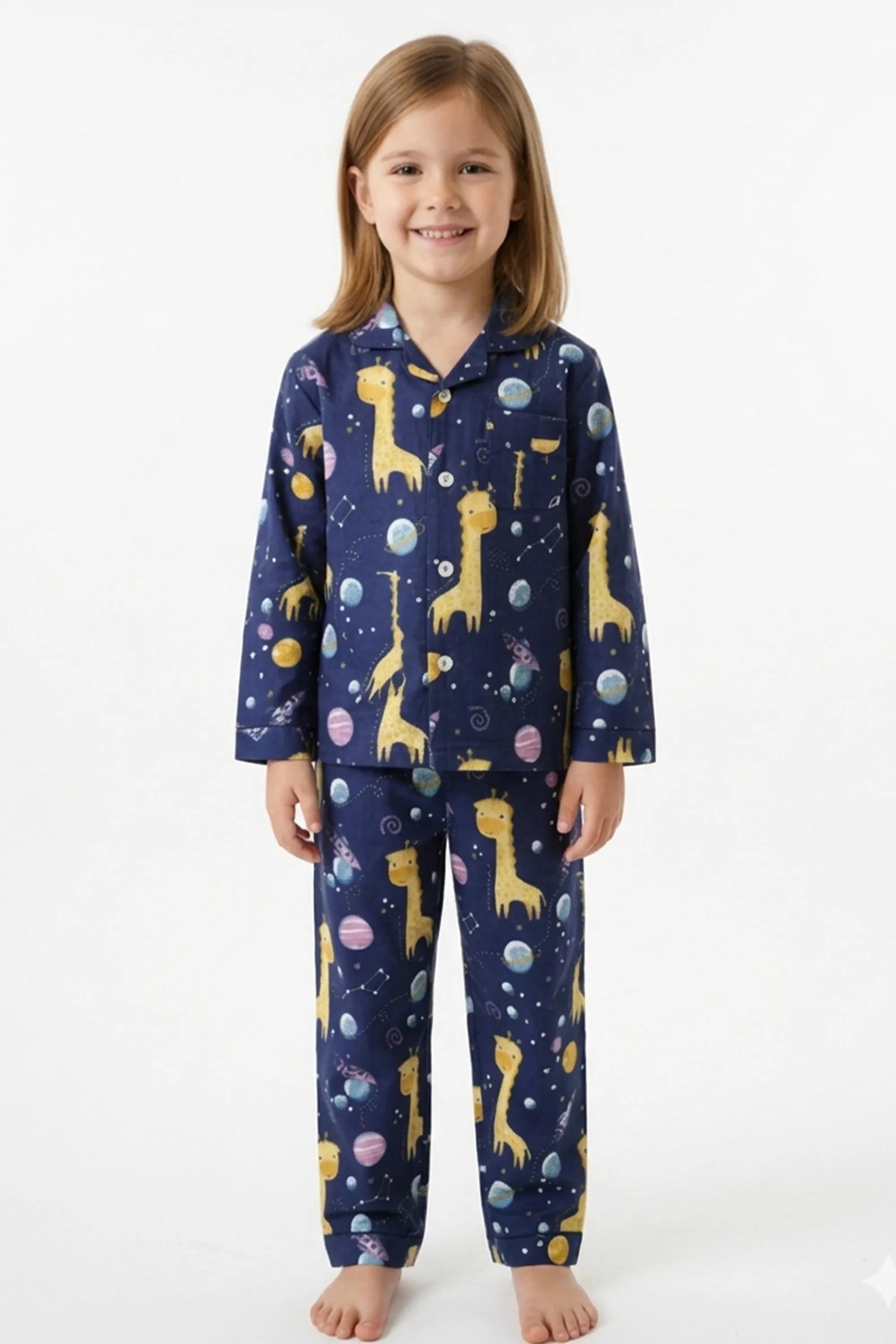 A young girl standing against a white background, wearing a navy blue long-sleeved button-up pajama set with a yellow giraffe and planet print