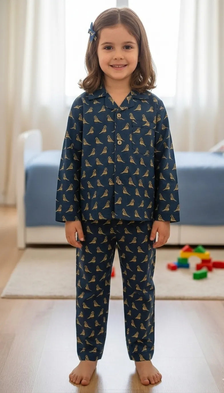 A young girl smiling while wearing a navy blue long-sleeved pajama set featuring an all-over golden-yellow bird pattern, standing in a brightly lit room.