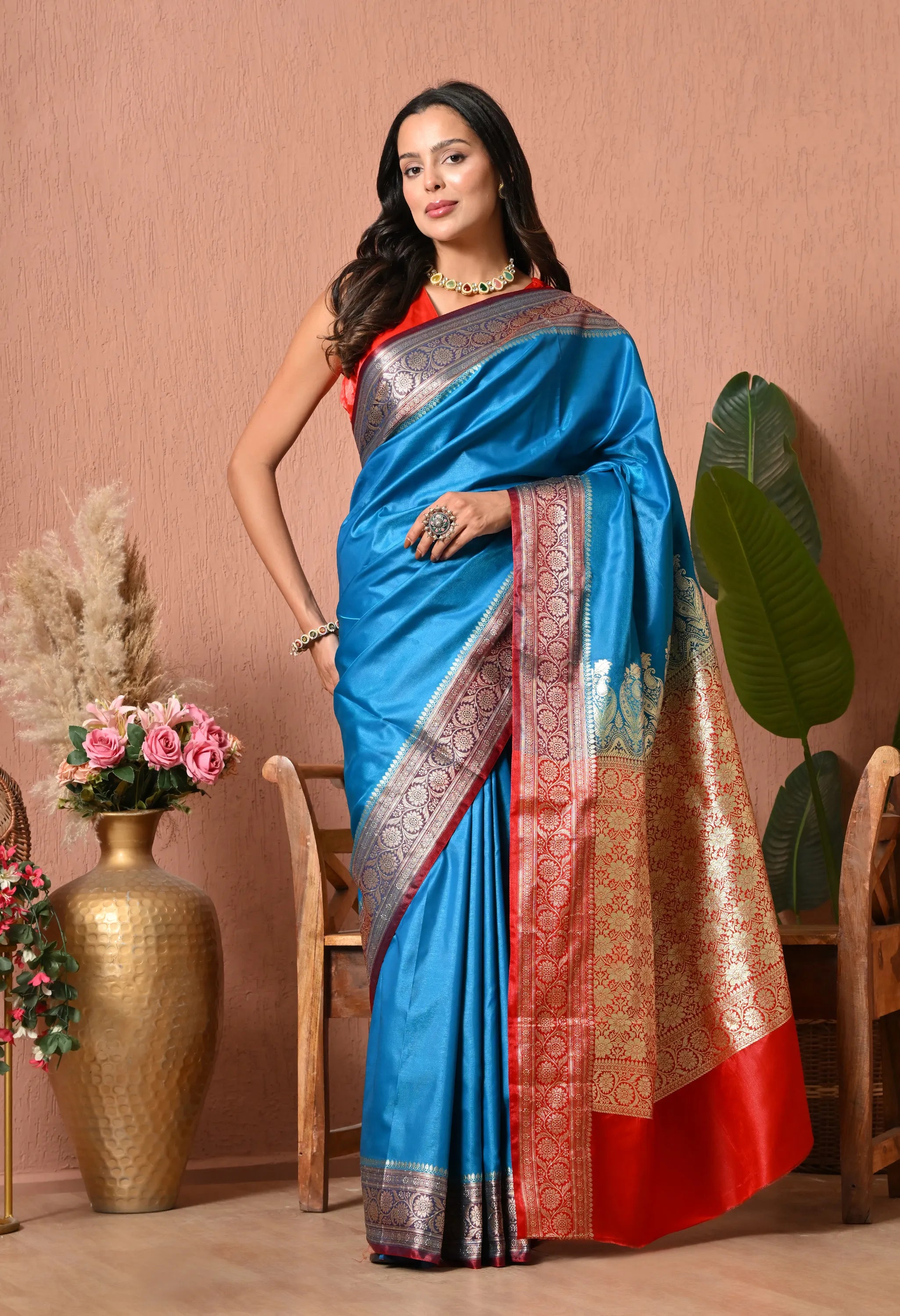 A woman modeling a luxurious feroza blue silk blend saree featuring a contrasting rich red border and grand pallu adorned with intricate golden zari weaving.
