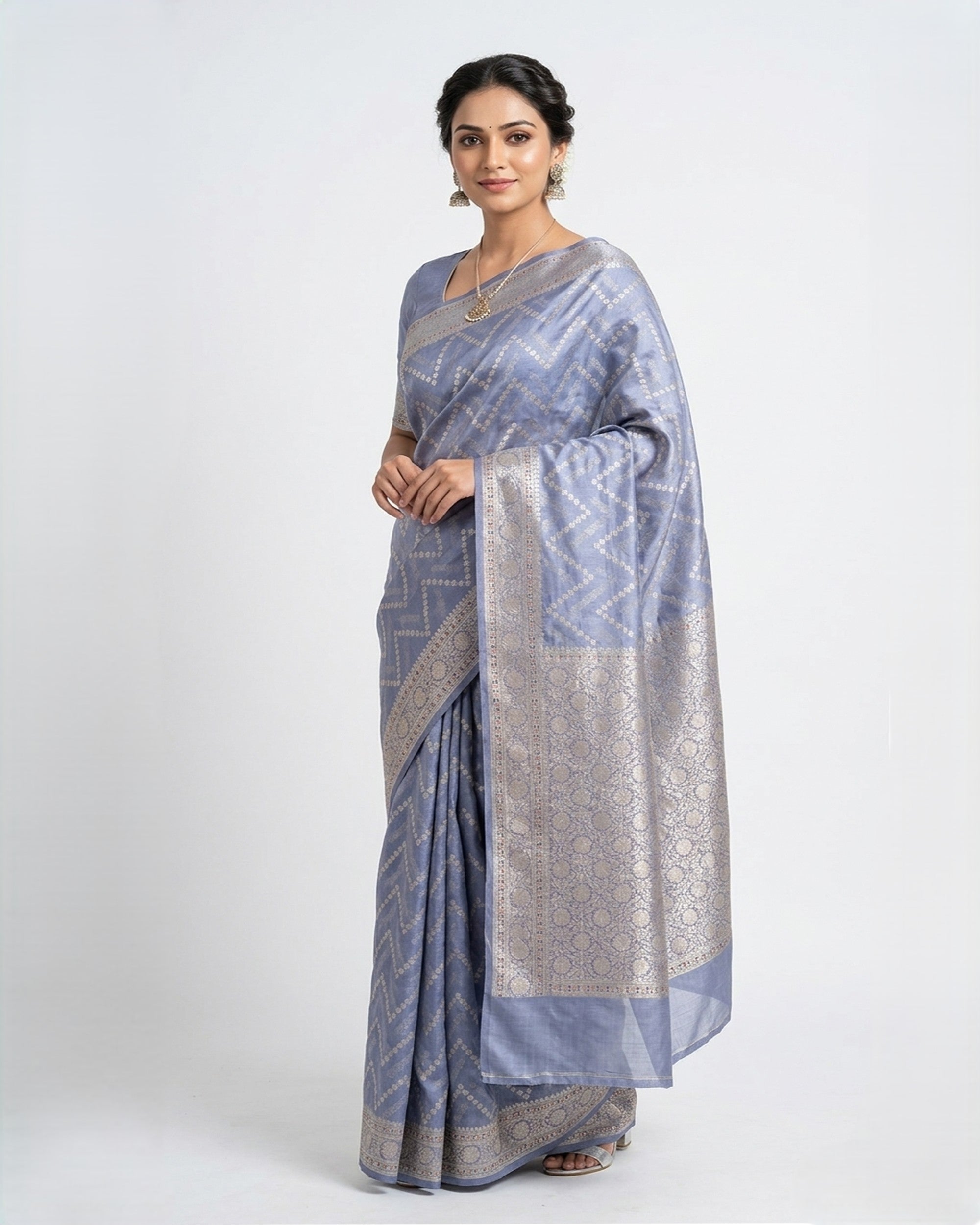 A woman wearing a light blue Banarasi silk saree with silver zari floral patterns and a broad, decorative border, posed against a plain white background
