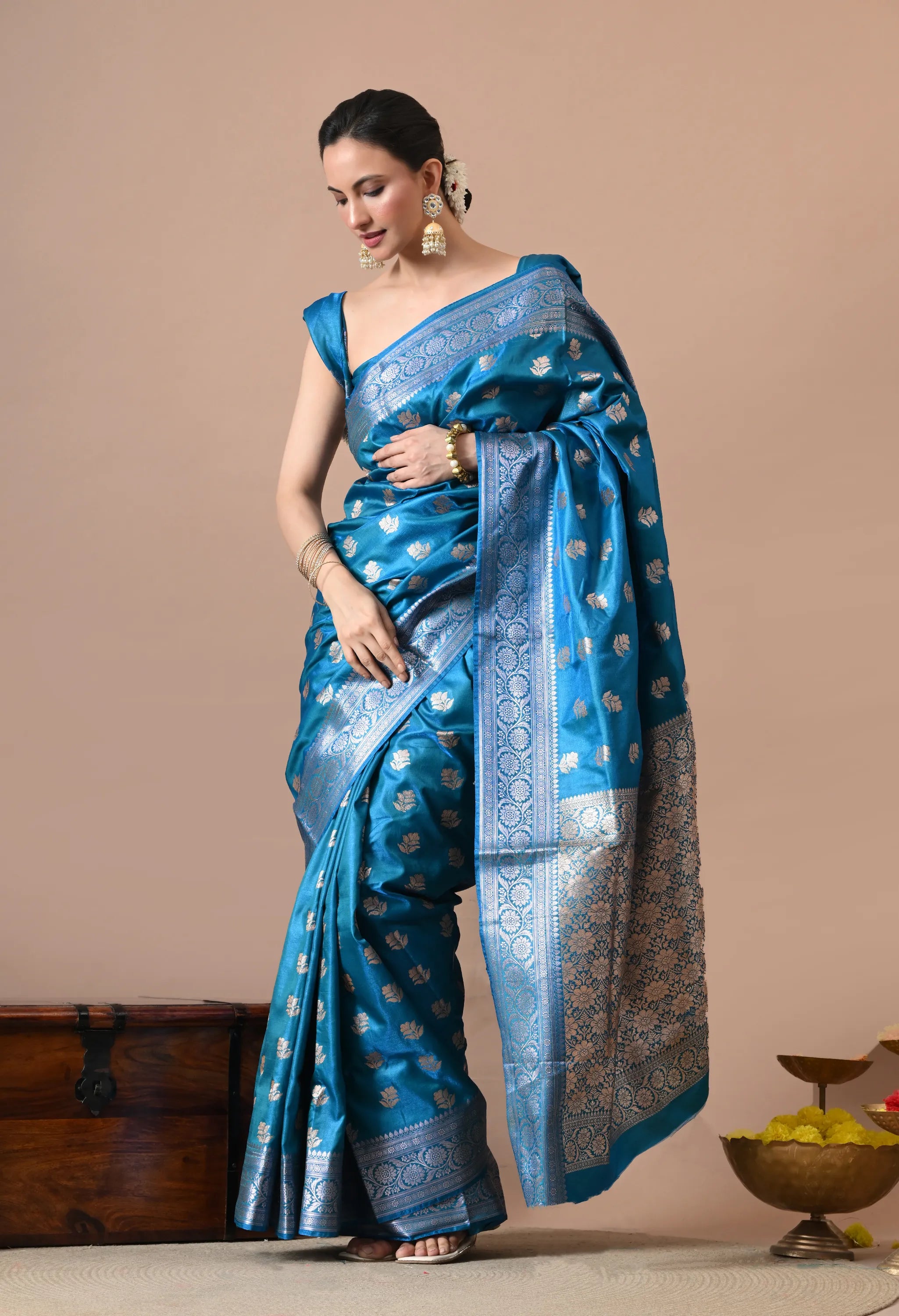 Woman wearing a teal blue silk-blend Banarasi saree with silver floral woven designs and a wide border.
