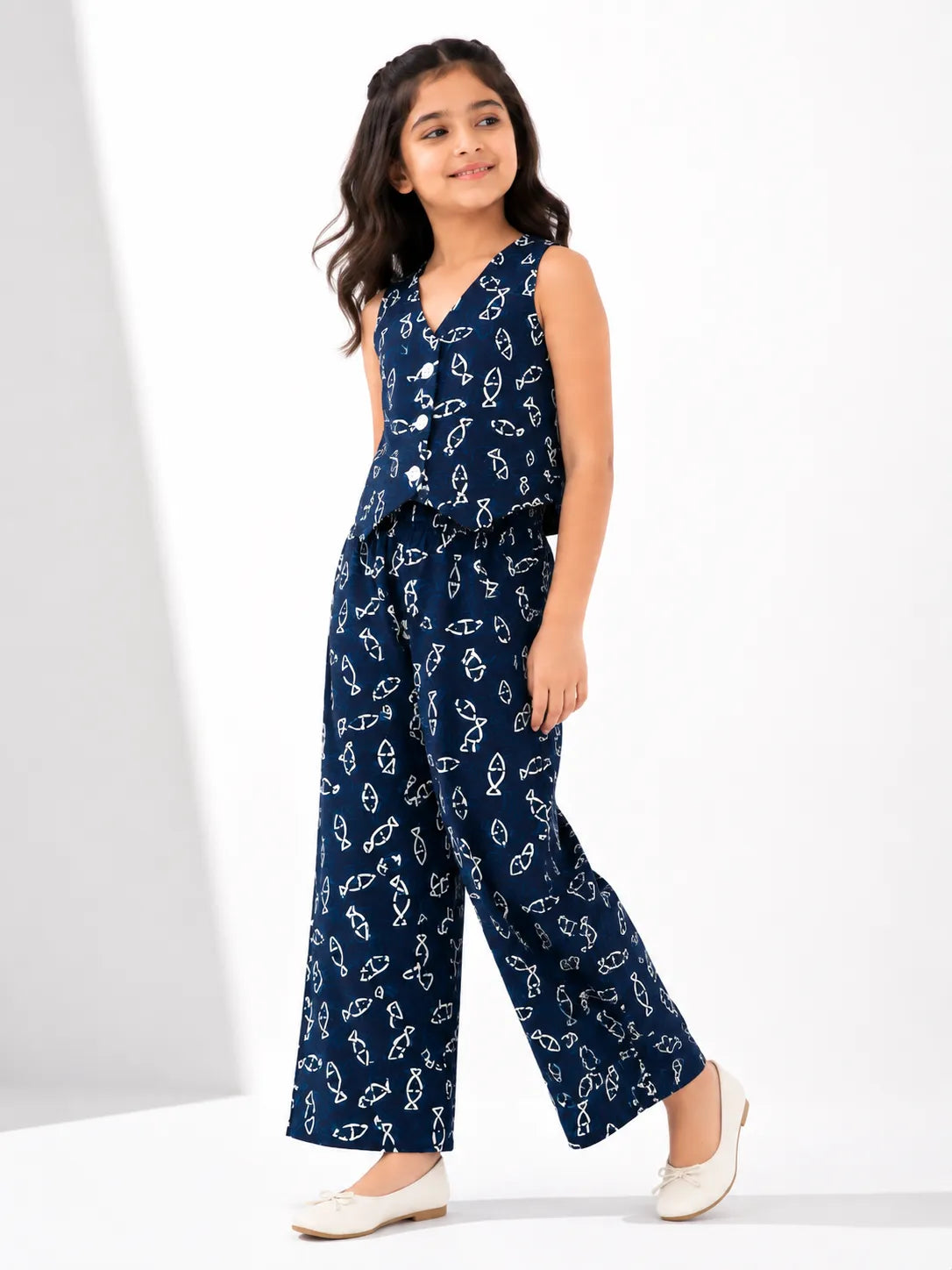 Young girl smiling while wearing a navy blue and white fish-printed co-ord set with a sleeveless vest and wide-leg pants.
