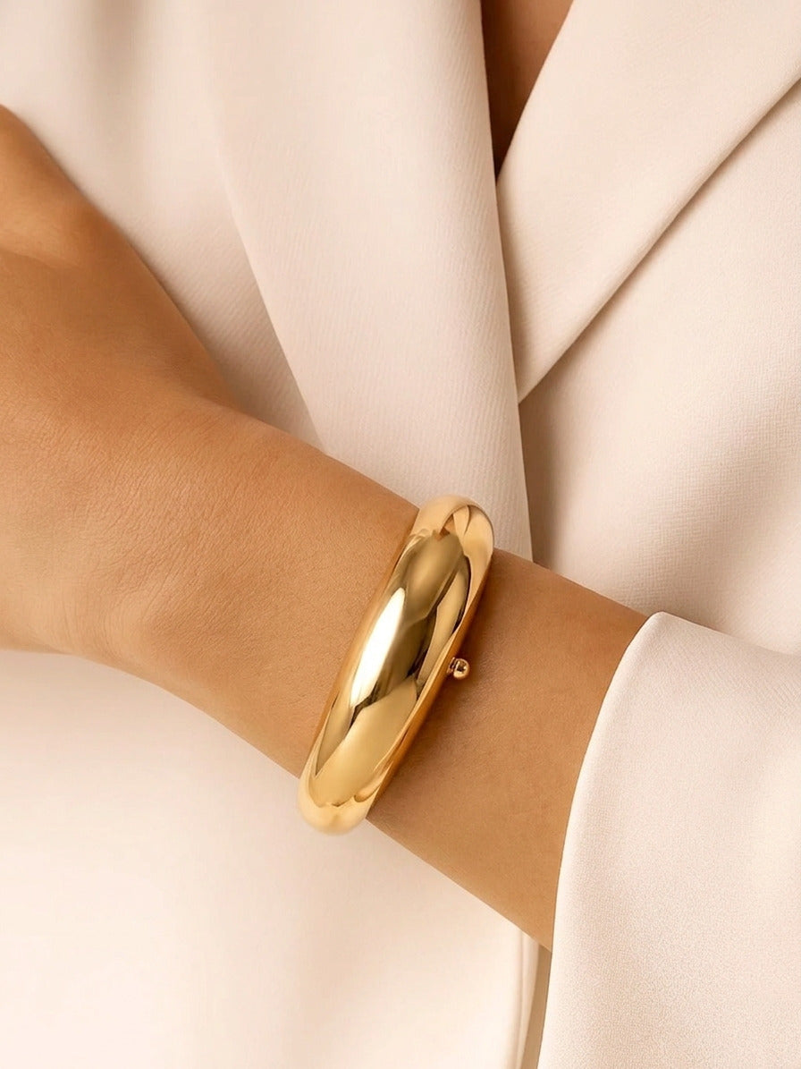 A high-shine chunky gold tapered bangle with a hinged closure, displayed on a plain white surface.