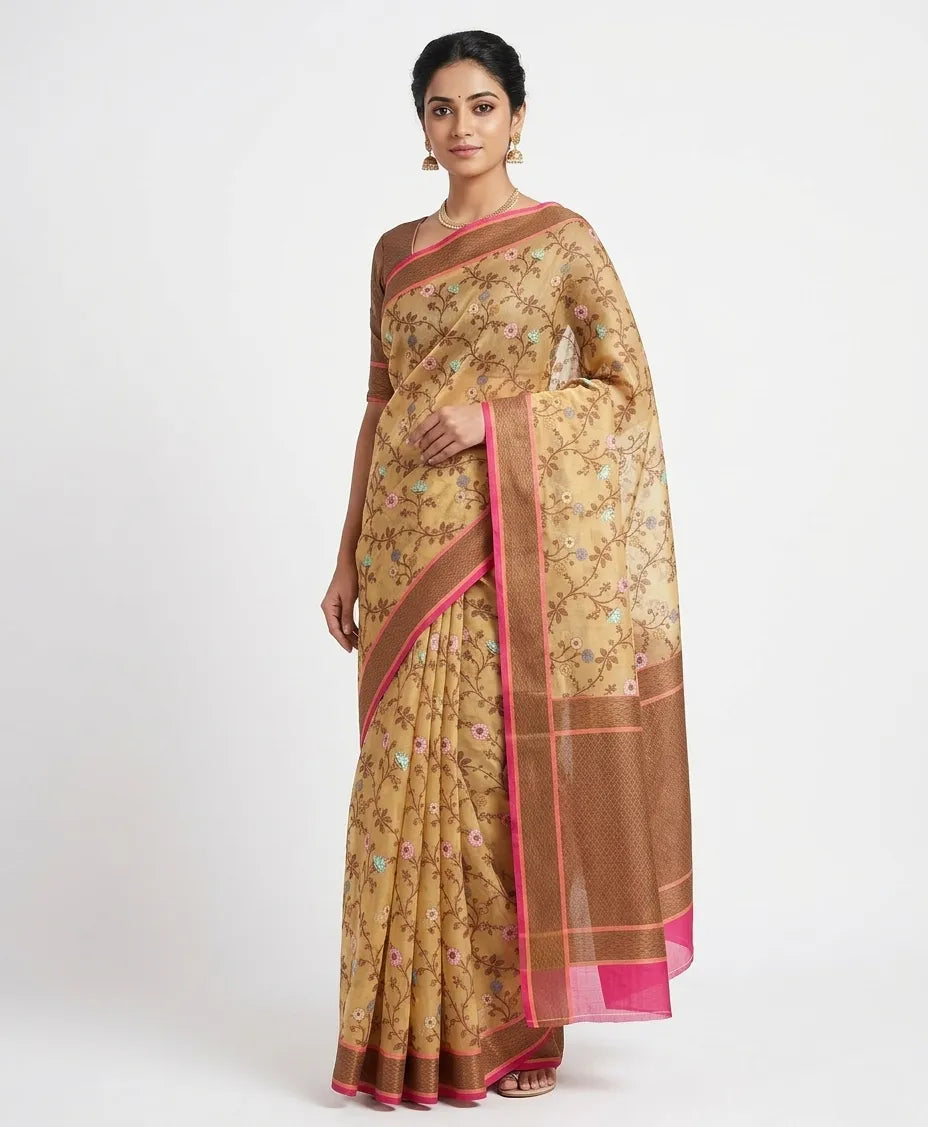 An Indian woman posing in a dusty pink silk blend saree featuring cream geometric woven patterns and a zari border. She is wearing a matching half-sleeved blouse and a gold necklace against a white background.
