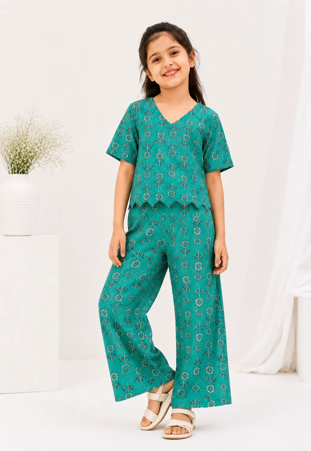 Young girl posing in a teal green floral printed two-piece co-ord set with a V-neck scallop-hem top and wide-leg trousers.
