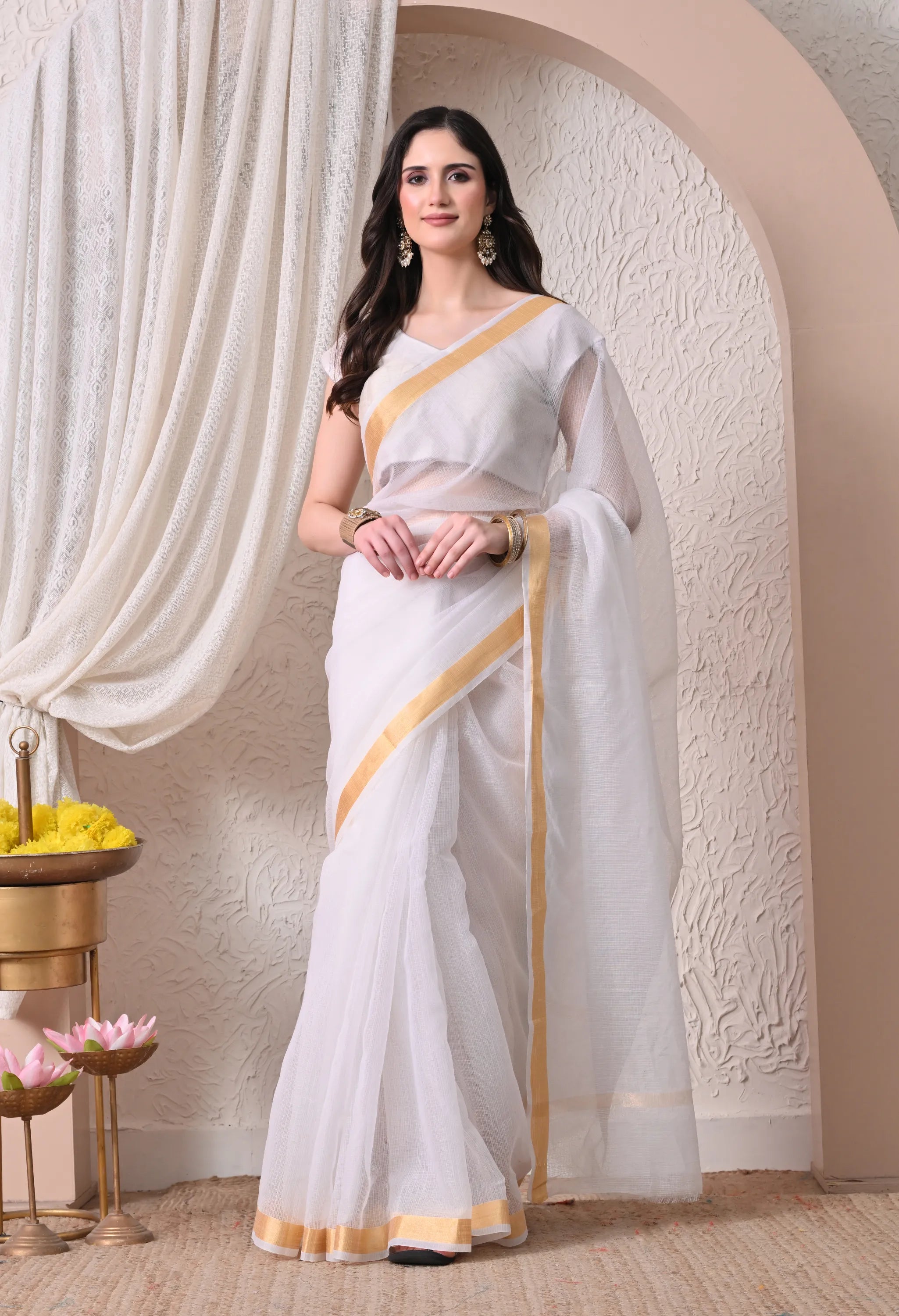 A woman modeling a sheer off white cotton saree featuring a simple, elegant golden zari border.
