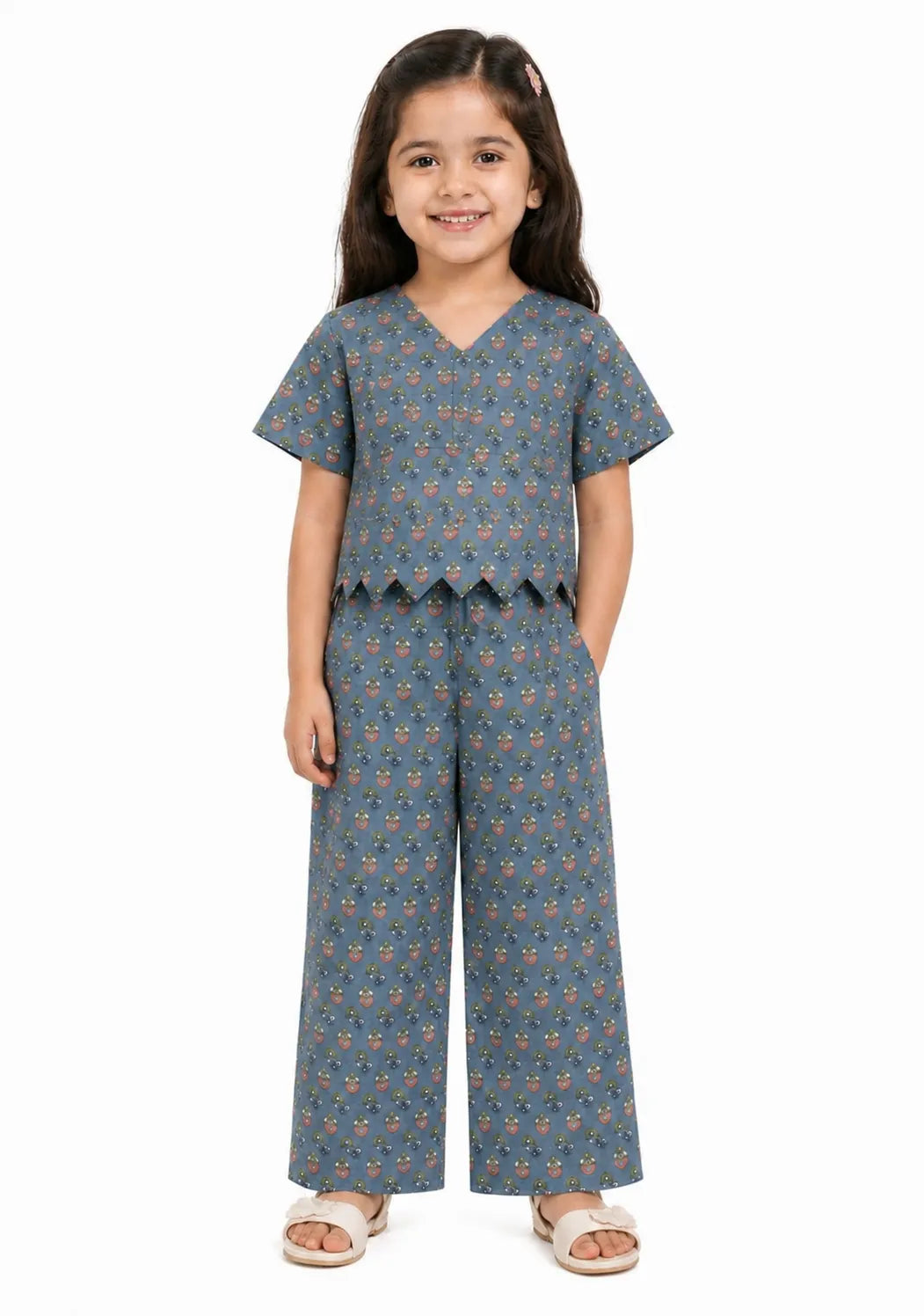 Young girl wearing a grey-blue floral printed cotton co-ord set with a scalloped hem top and wide-leg trousers.
