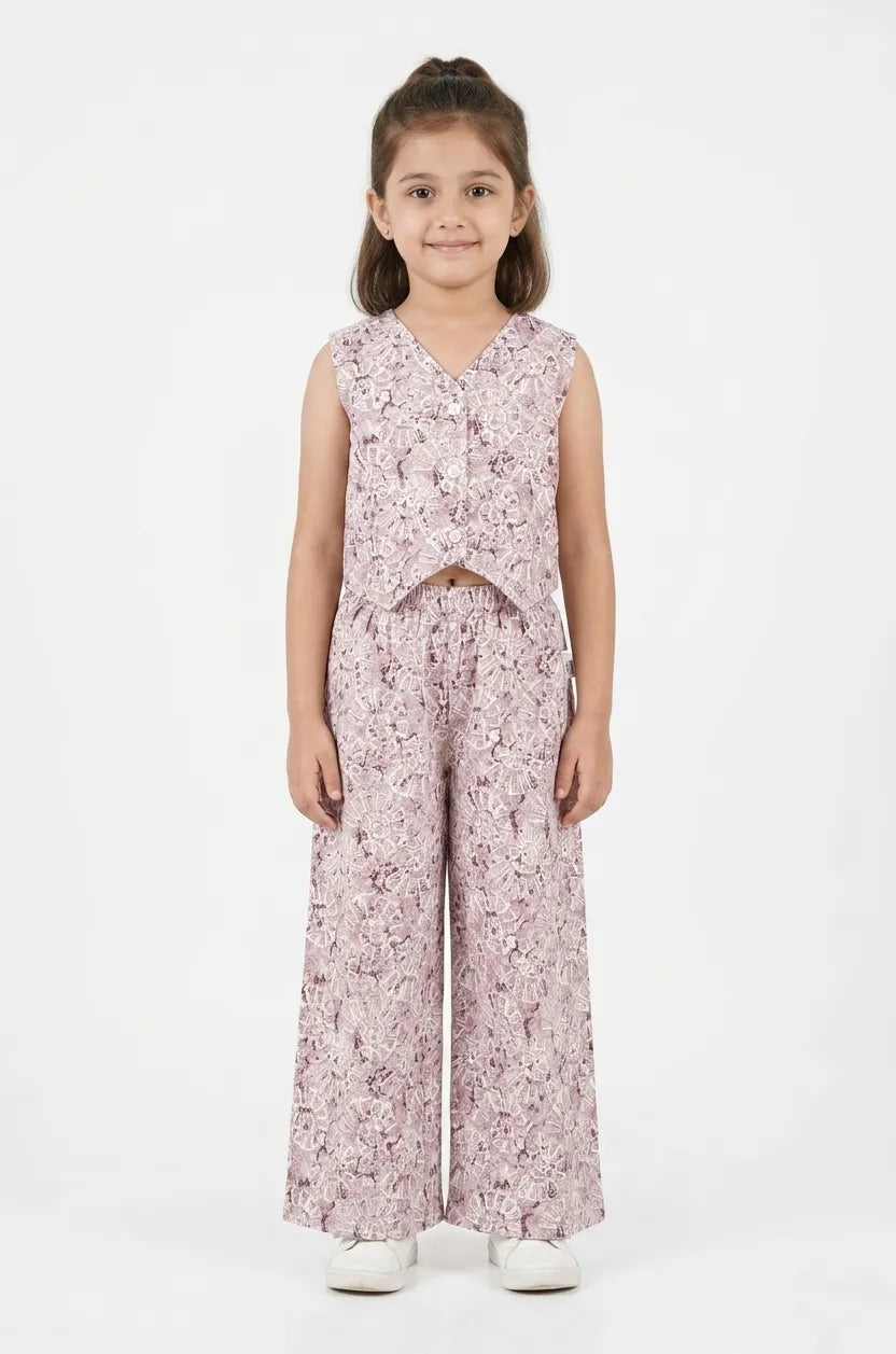 Young girl wearing a mauve and white floral printed cotton co-ord set featuring a sleeveless button-up top and wide-leg trousers.
