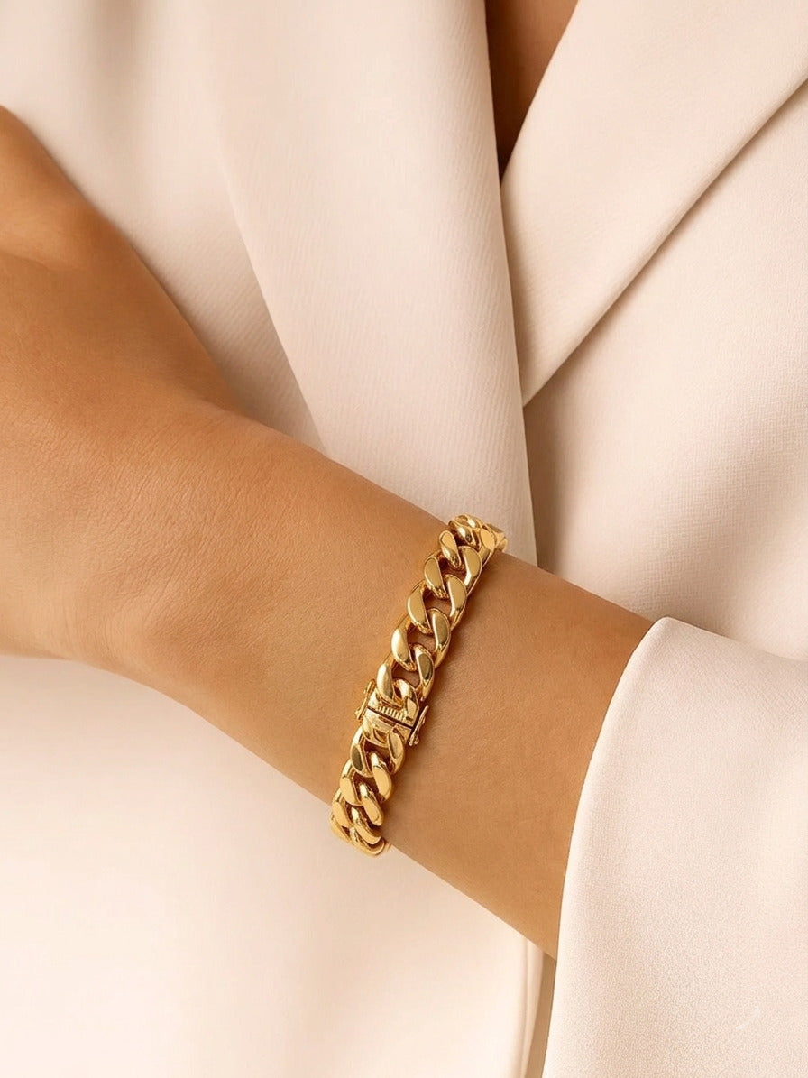 A thick, polished gold curb chain bracelet worn on a wrist, featuring a classic interlinked design with a high-shine finish against a neutral background.