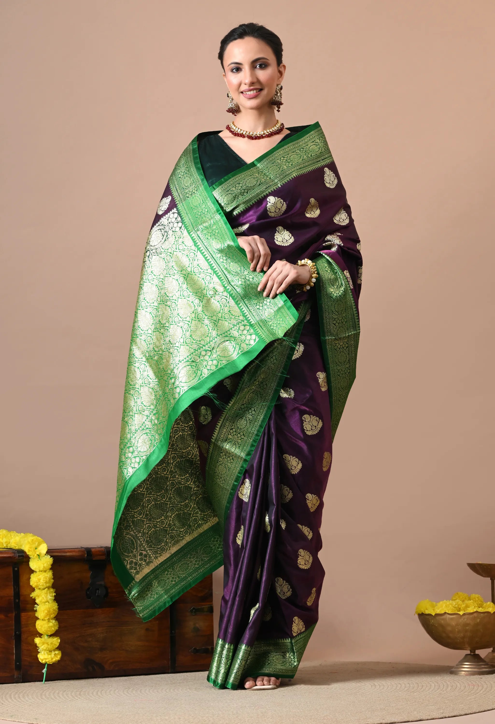 Woman wearing a deep purple and green silk-blend Banarasi saree with gold woven motifs and a contrast border.
