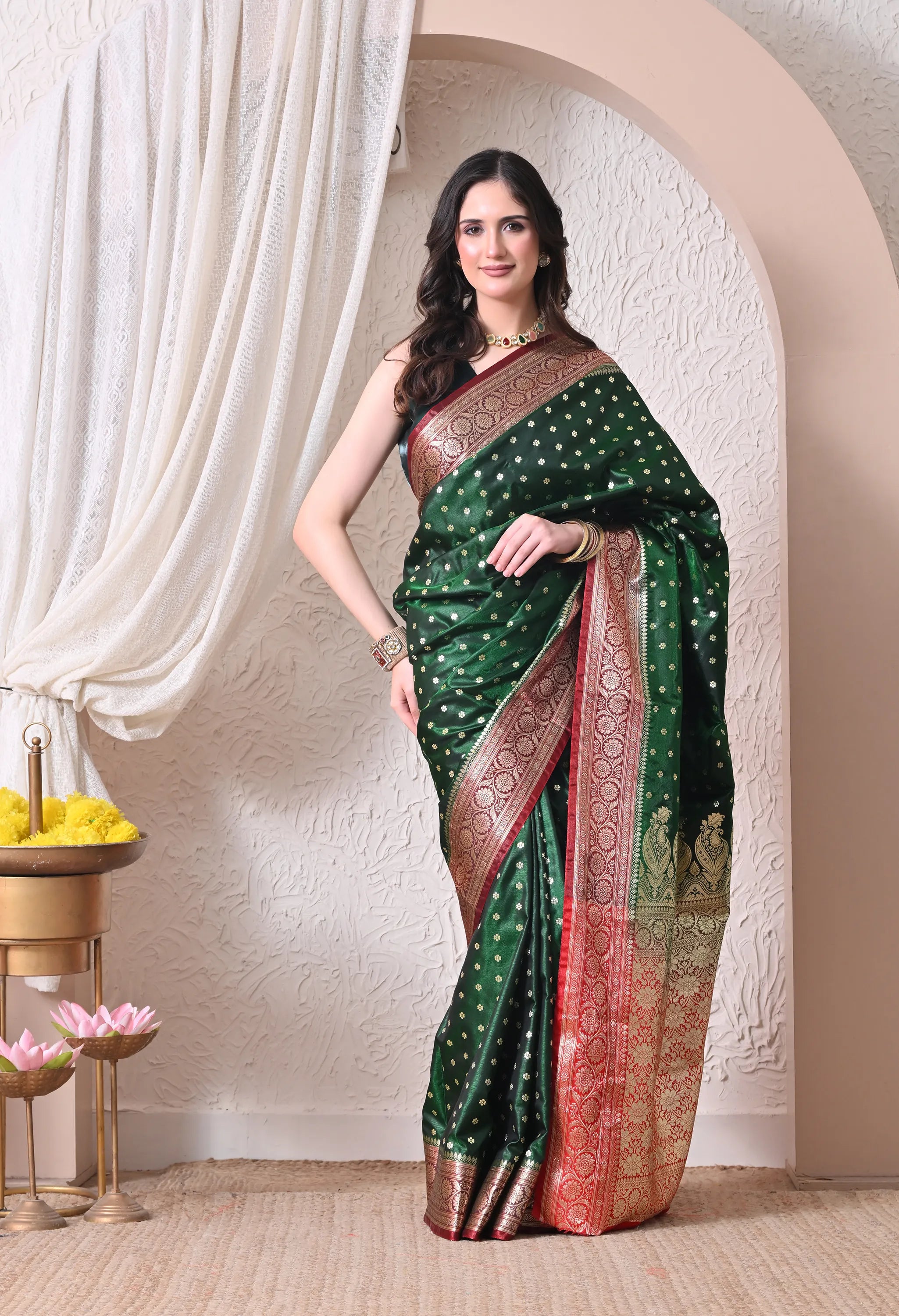 A woman modeling a deep bottle green silk blend Banarasi saree with small gold zari motifs, featuring a thick contrast maroon and gold intricate woven border and pallu.
