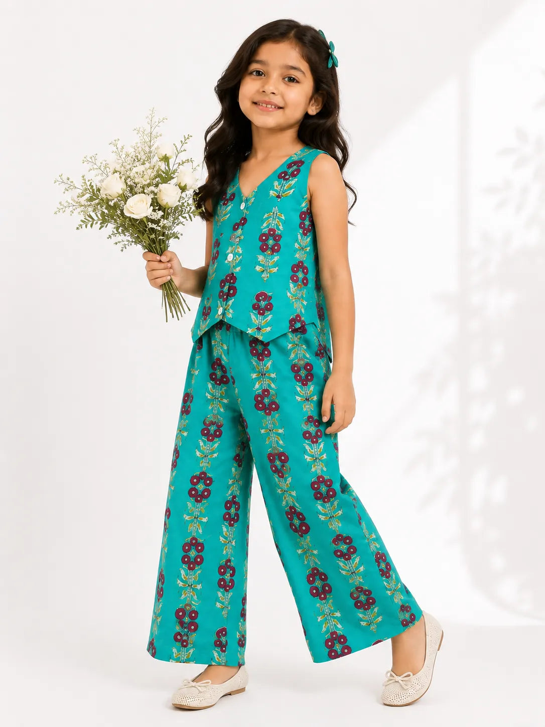 Young girl posing in a turquoise blue two-piece co-ord set with maroon floral block prints, featuring a sleeveless buttoned top and wide-leg trousers.
