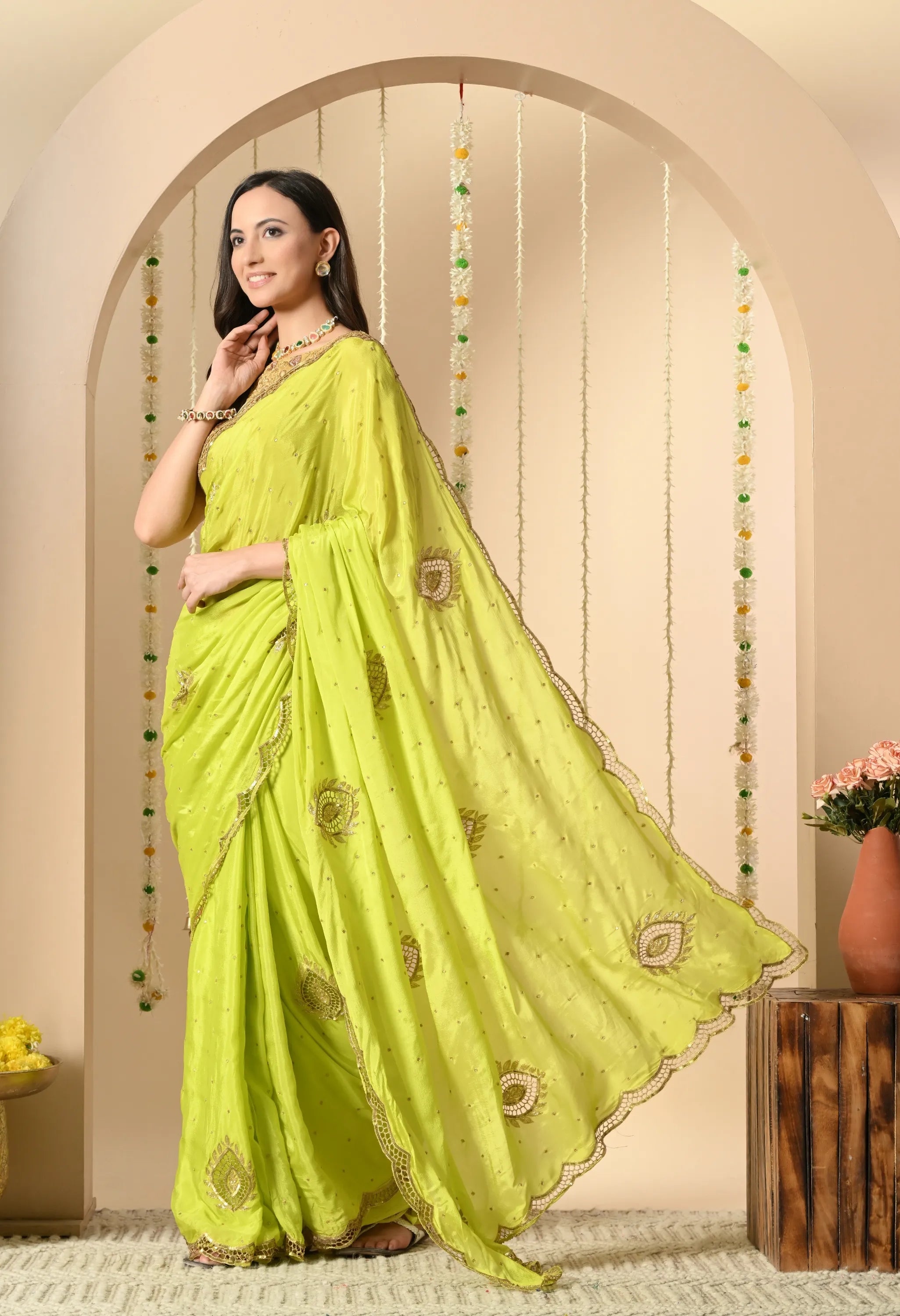 Side profile of a model showcasing the elegant flare of an acid-green crepe saree from The Weavers Shop by Raavi. The image highlights the intricate scalloped hand-cut work along the borders, drop zardozi hand-embroidery motifs with cut work, and the lightweight, flowing drape of the chiffon fabric.