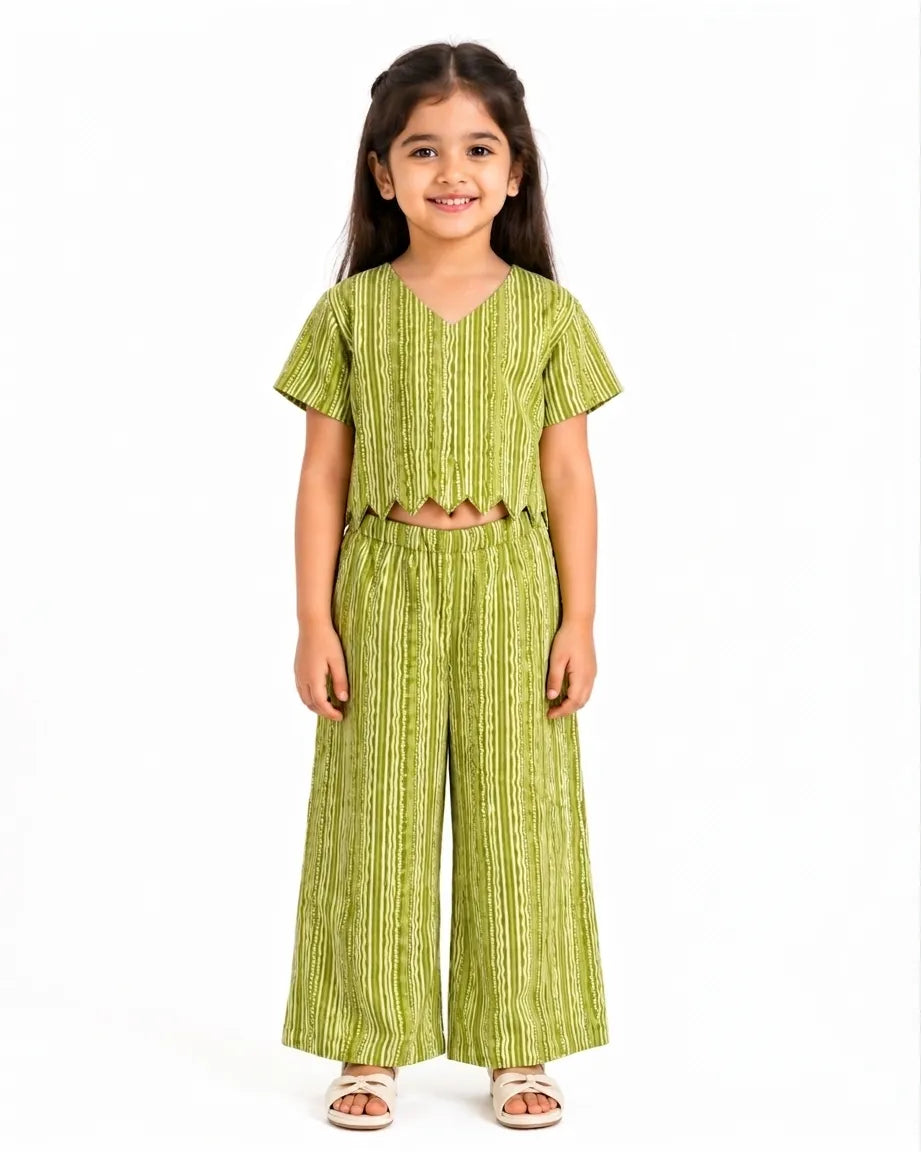 A young girl modeling a vibrant lime green and white striped ethnic co-ord set. The outfit consists of a short-sleeved V-neck crop top with a decorative scalloped hemline and matching wide-leg vertical striped trousers, set against a solid white background.
