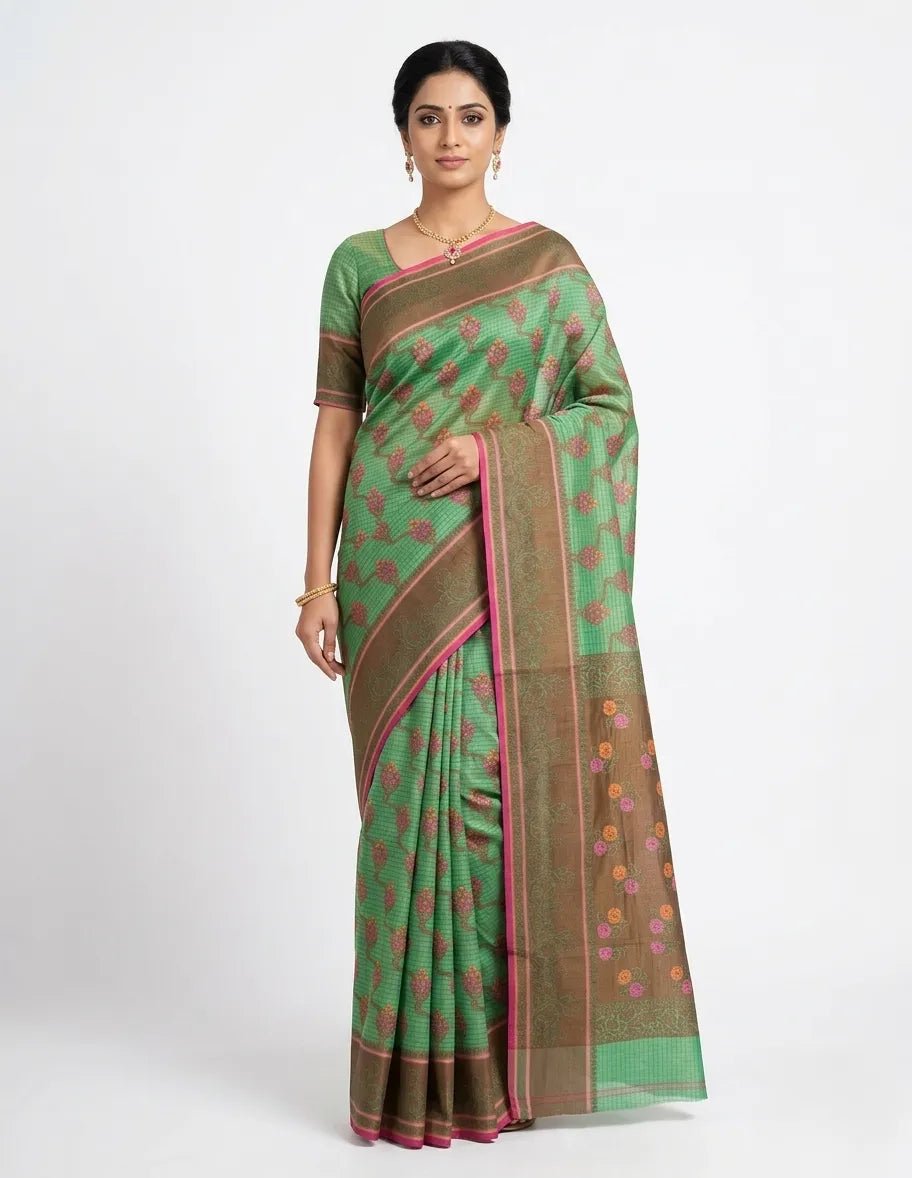 Woman posing in a sea green checked silk blend saree with brown borders and pink floral woven motifs.
