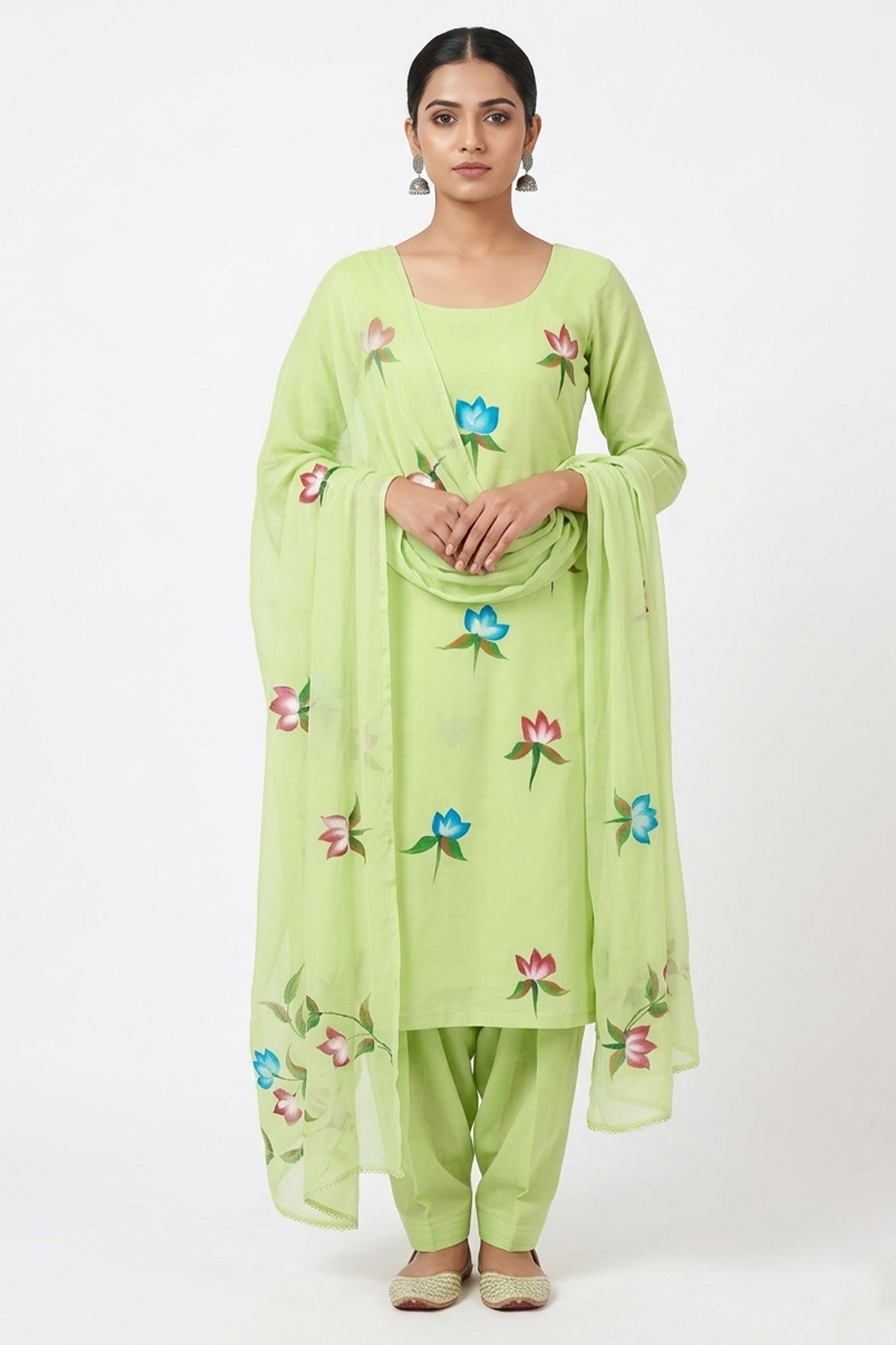 Woman wearing a light lime green unstitched suit with hand-painted floral motifs in blue and pink, featuring a matching dupatta and salwar on a plain white background.