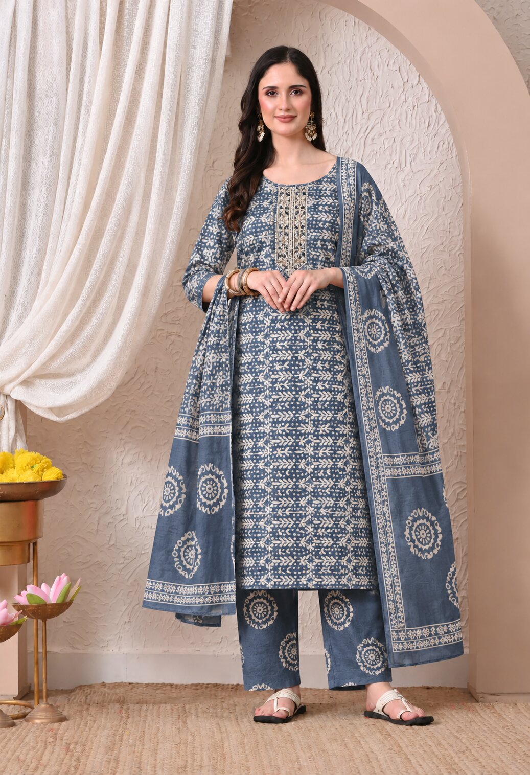 Blue-grey ethnic kurta suit with intricate white geometric prints, round neckline with decorative embroidery, matching printed trousers, and a coordinating dupatta featuring traditional floral motifs and patterned borders.
