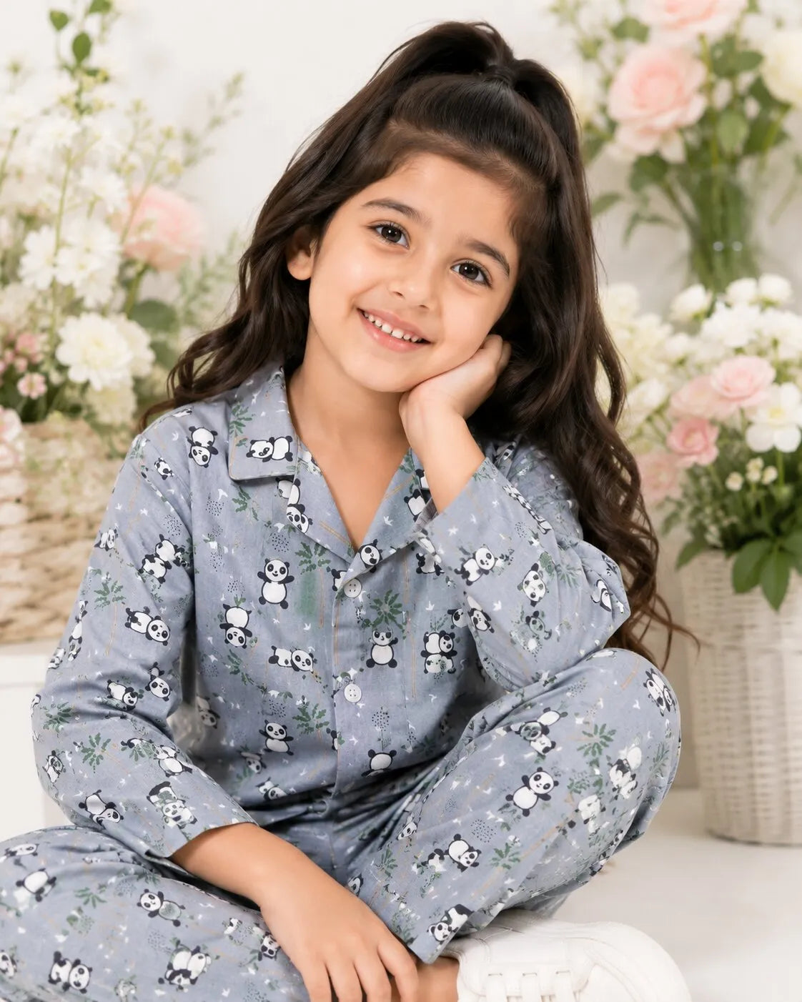 A young girl smiling while wearing a grey, long-sleeved night suit featuring an all-over black and white panda print with green bamboo accents.