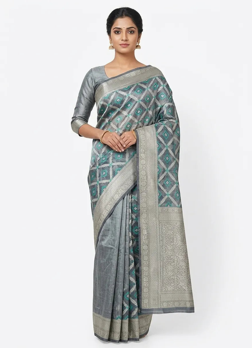 Model wearing a charcoal grey silk blend Banarasi saree featuring a teal and silver geometric diamond woven pattern and a broad silver zari border.