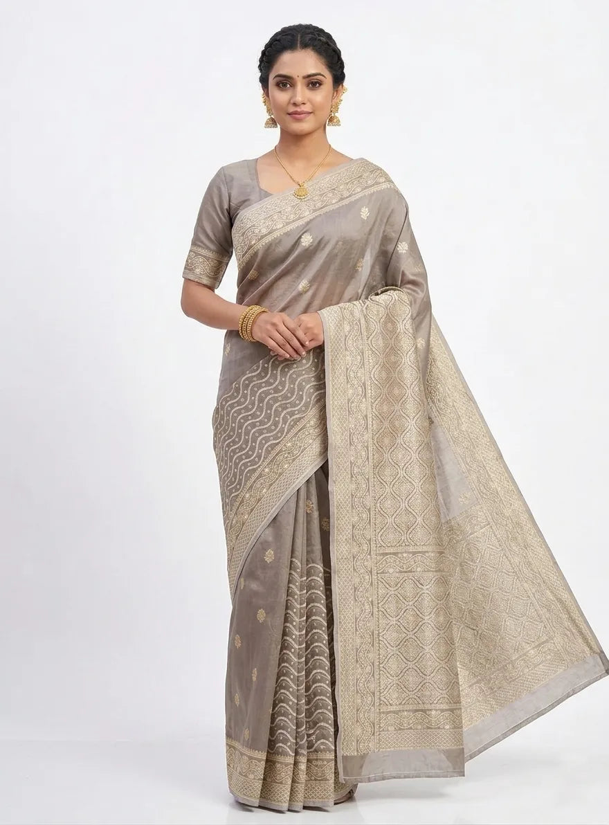 Woman in a grey Banarasi silk blend saree featuring gold Zari wavy patterns, floral buttis, and an ornate geometric pallu.