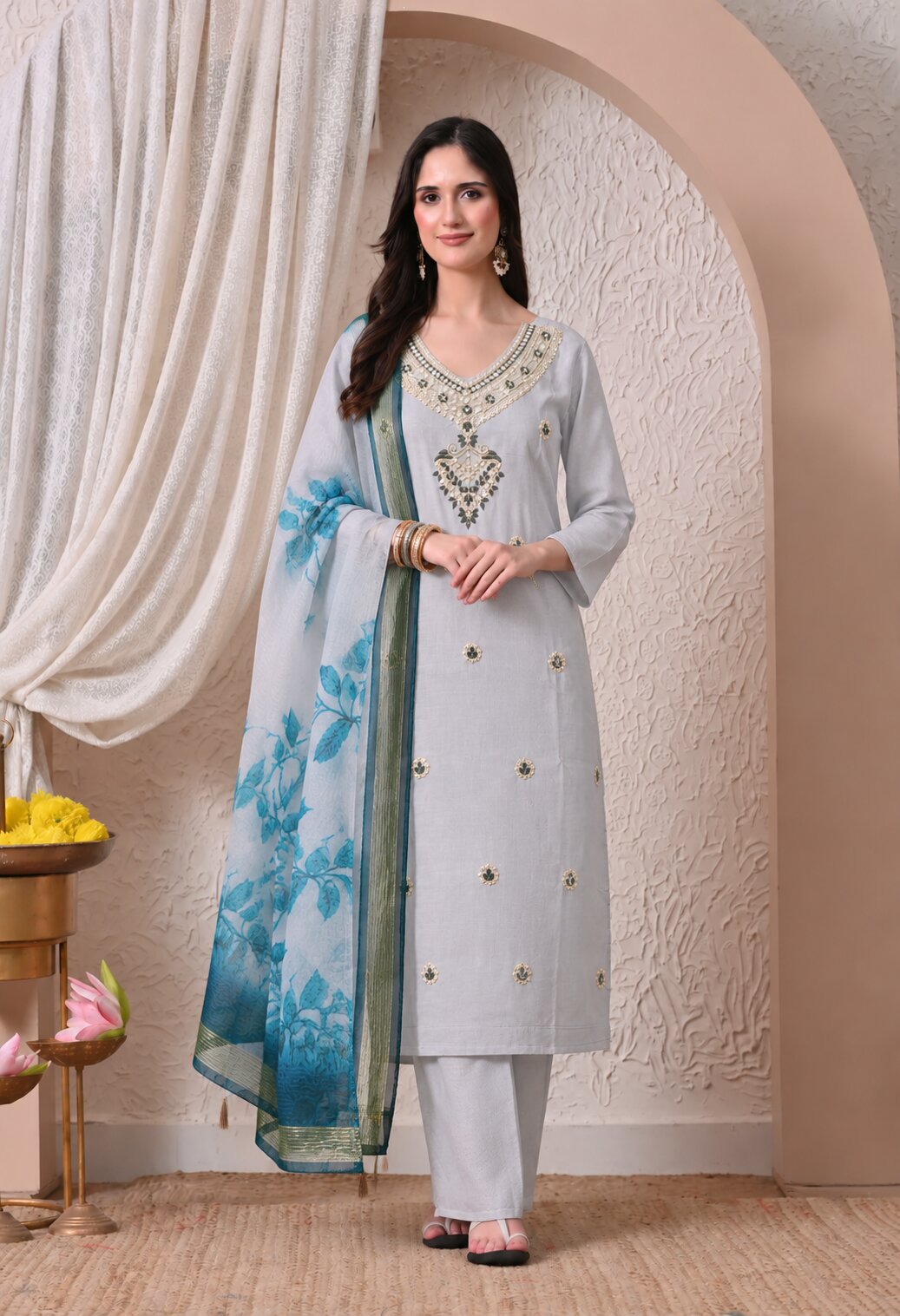 Light grey ethnic salwar suit set featuring a straight-cut kurta with intricate gold embroidery on the neckline and chest, small floral motifs, matching white trousers, and a blue floral printed dupatta with a decorative border.
