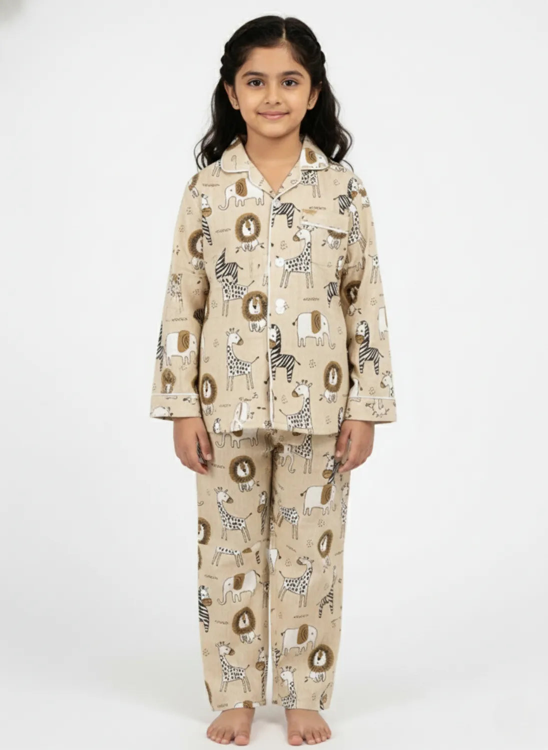 A young girl modeling a beige, long-sleeved pajama set featuring an all-over brown animal print, standing against a plain white background.