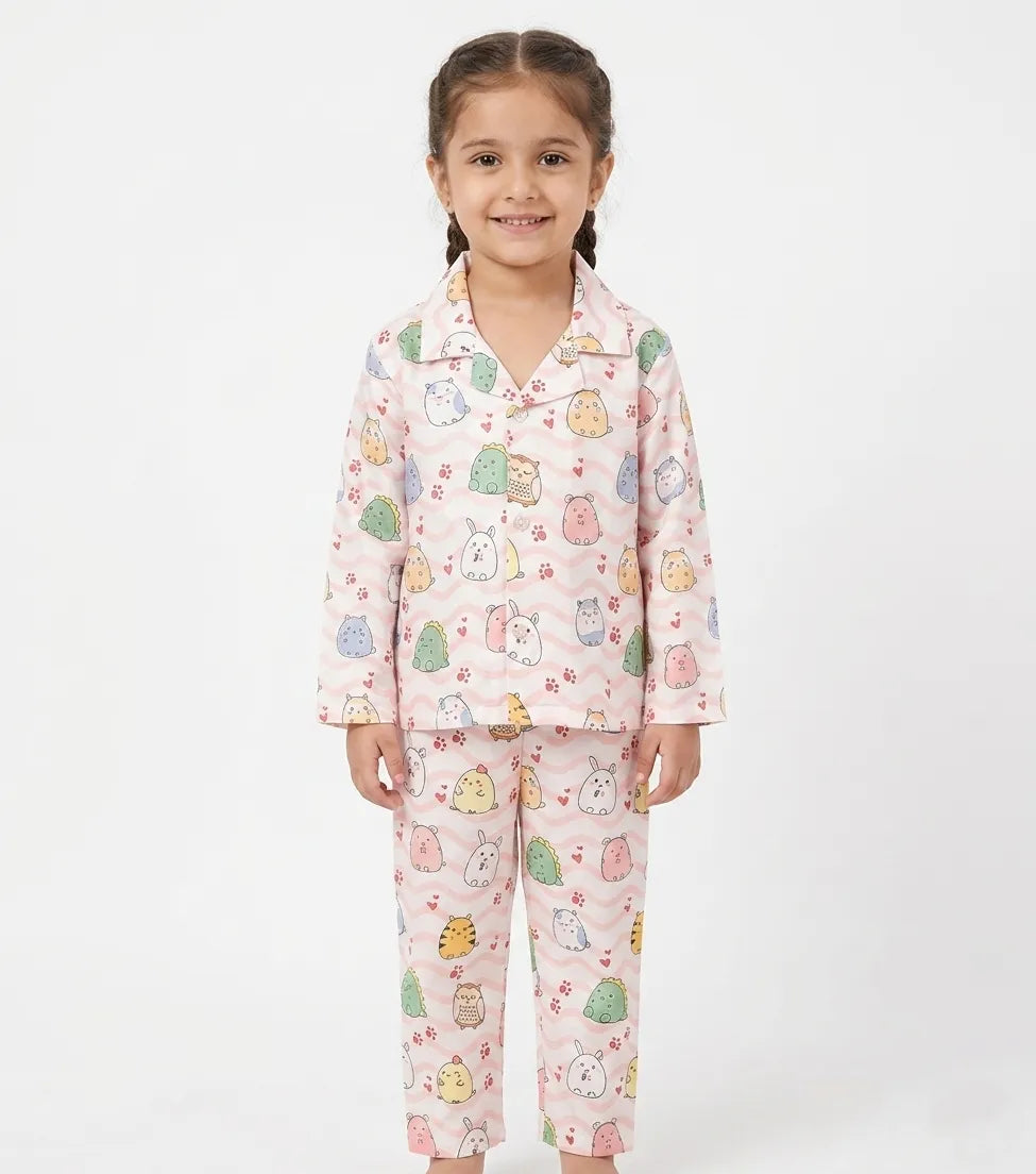 A young Girl standing in a light pink satin night suit featuring a colorful animal and wavy line print.
